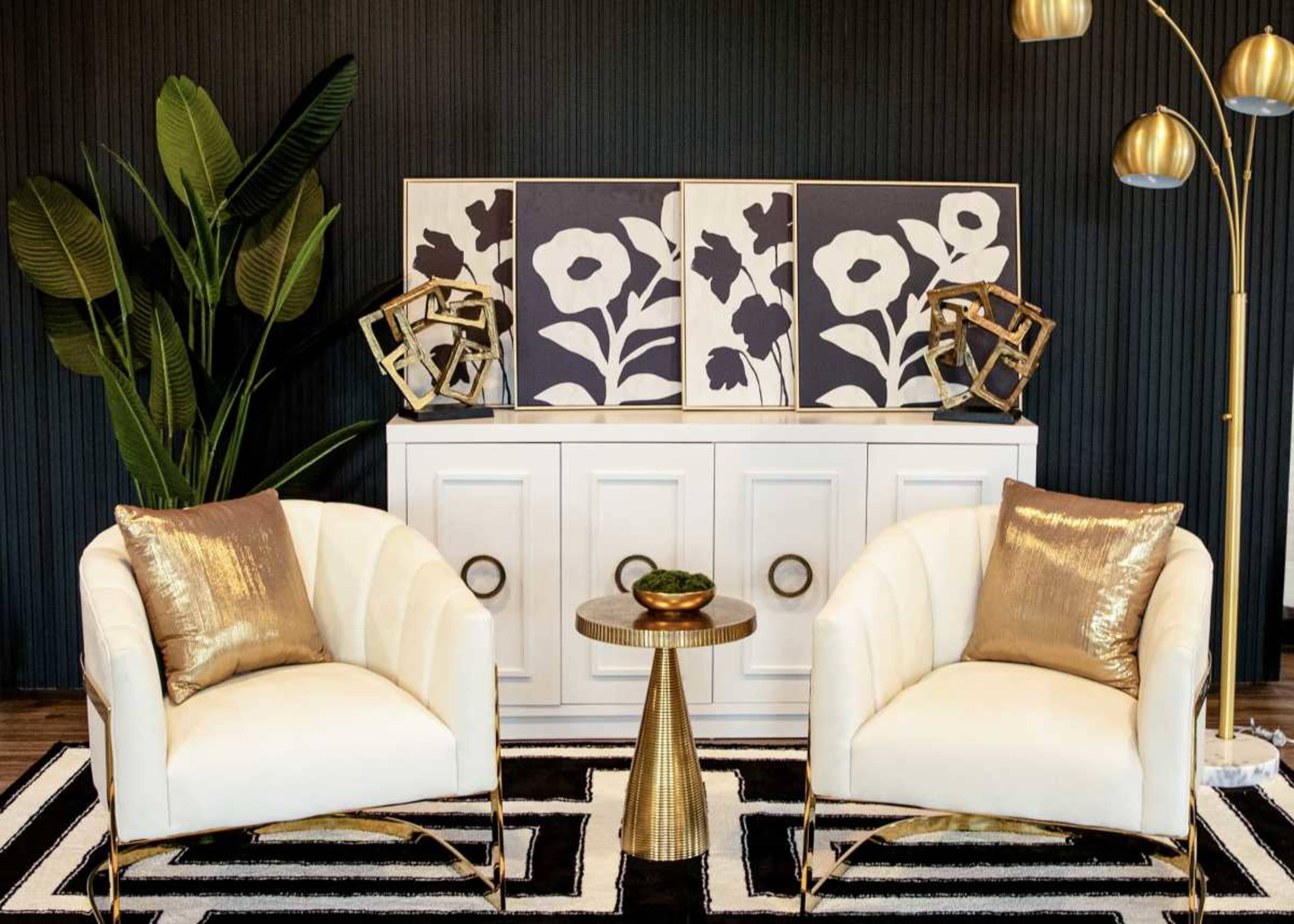 The image shows a modern living room setup featuring two white armchairs with gold accents, a small circular table, a decorative cabinet, and wall art, all arranged against a dark background.