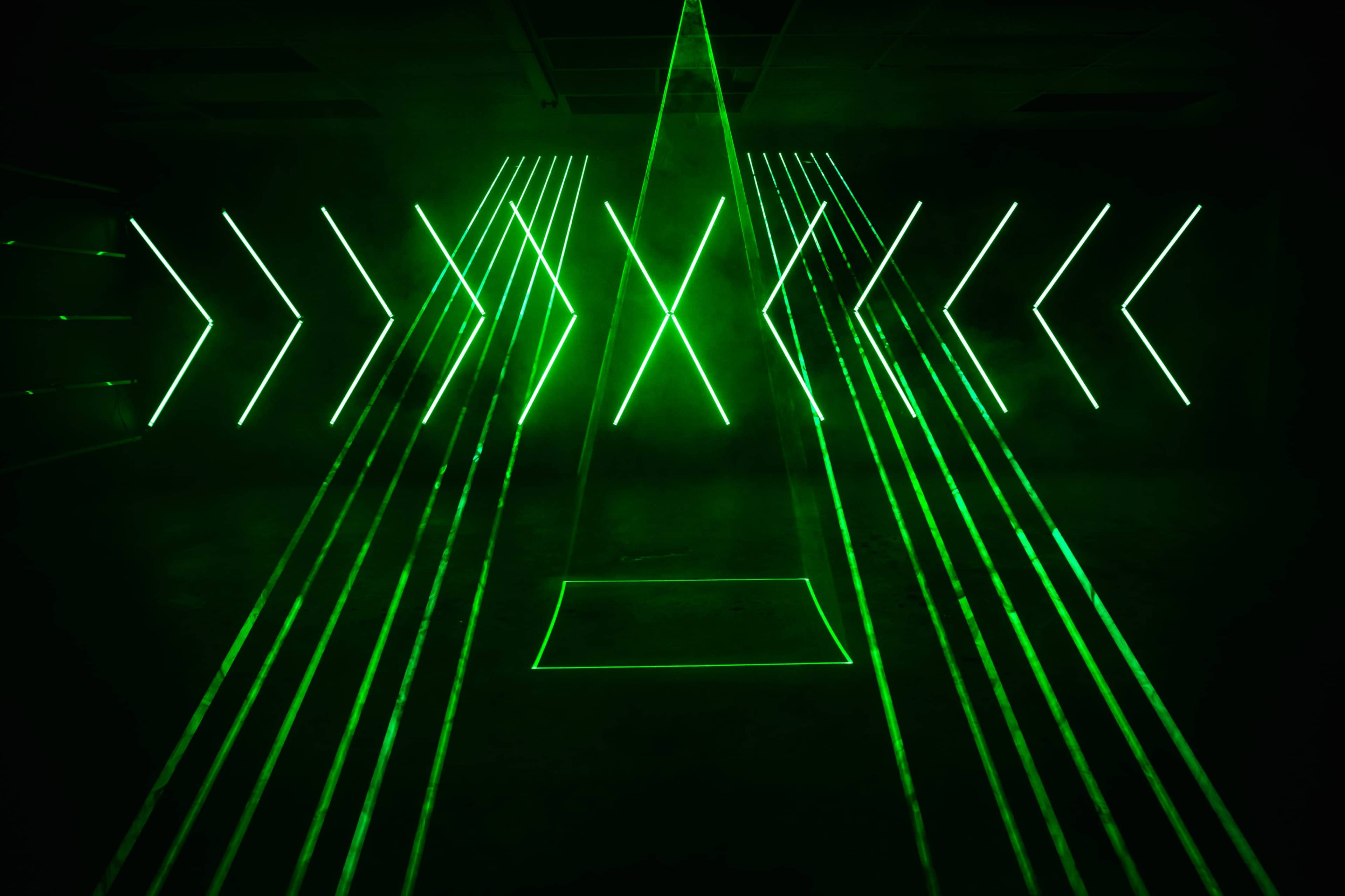 A dark room illuminated by bright green laser beams arranged in multiple diagonal and vertical lines.