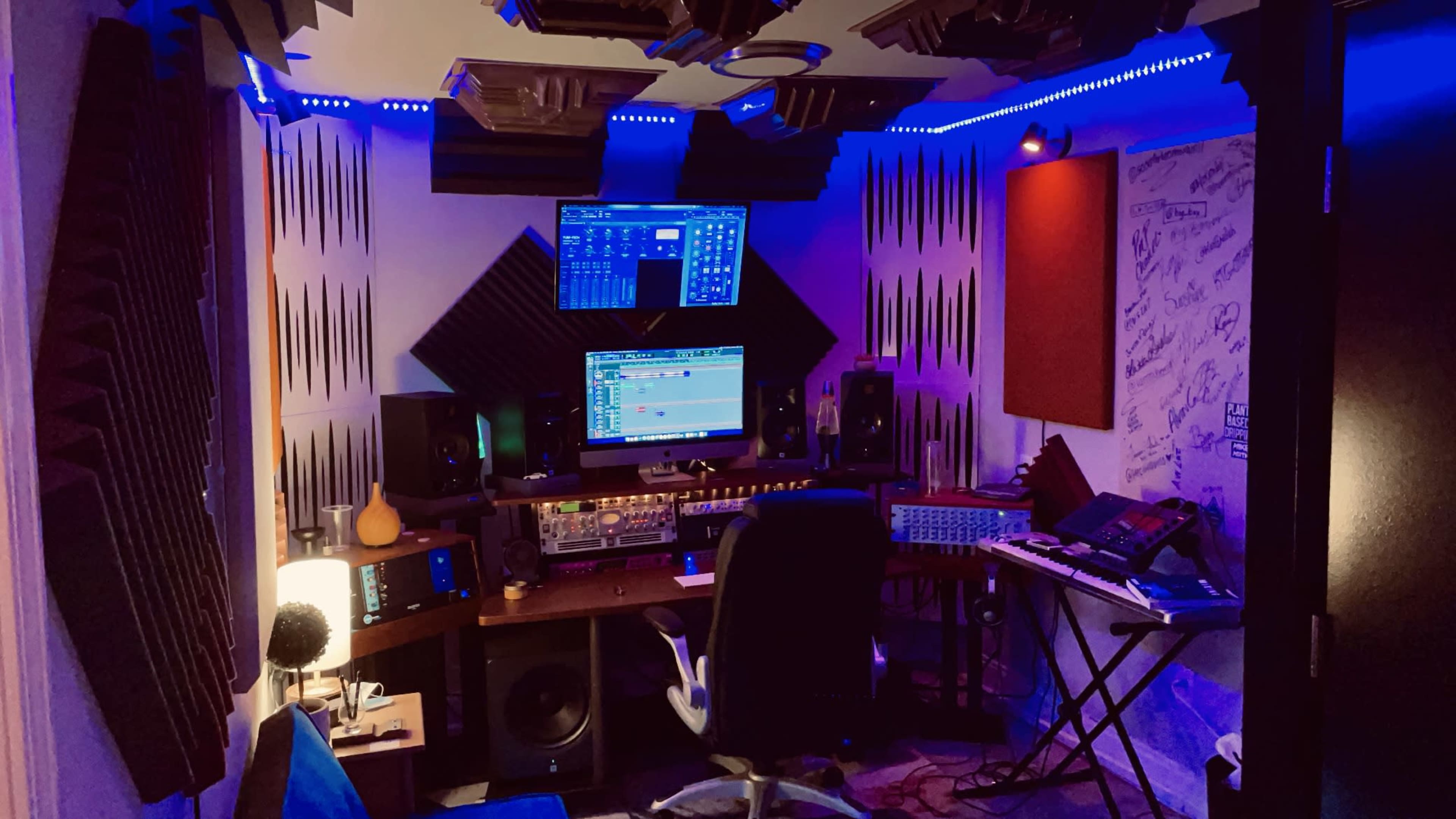 A music production studio equipped with multiple screens, audio equipment, and soundproofing panels on the walls.