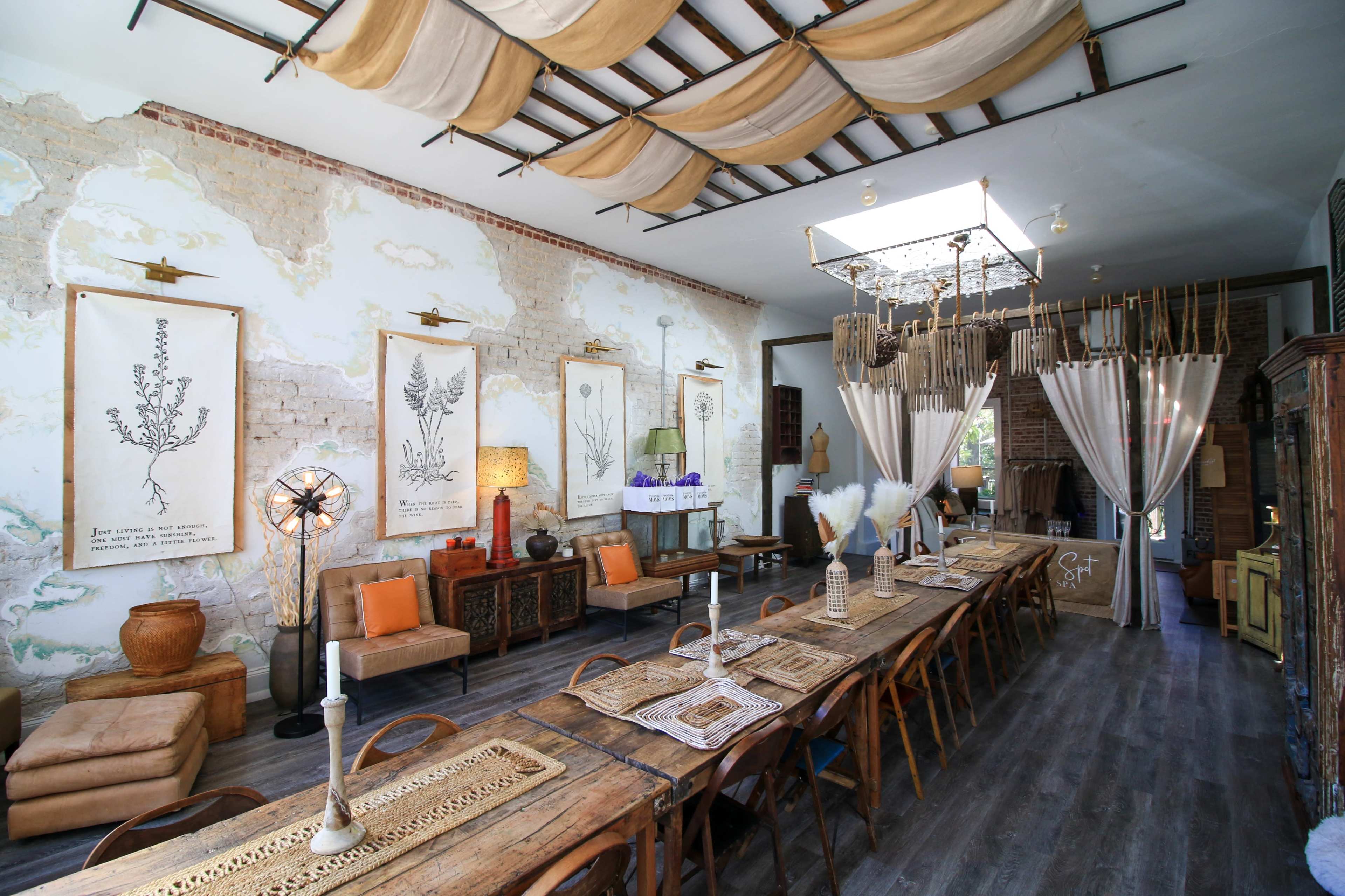 A spacious dining area featuring a long wooden table surrounded by various seating options, with botanical artwork displayed on the walls and soft lighting hanging from the ceiling.