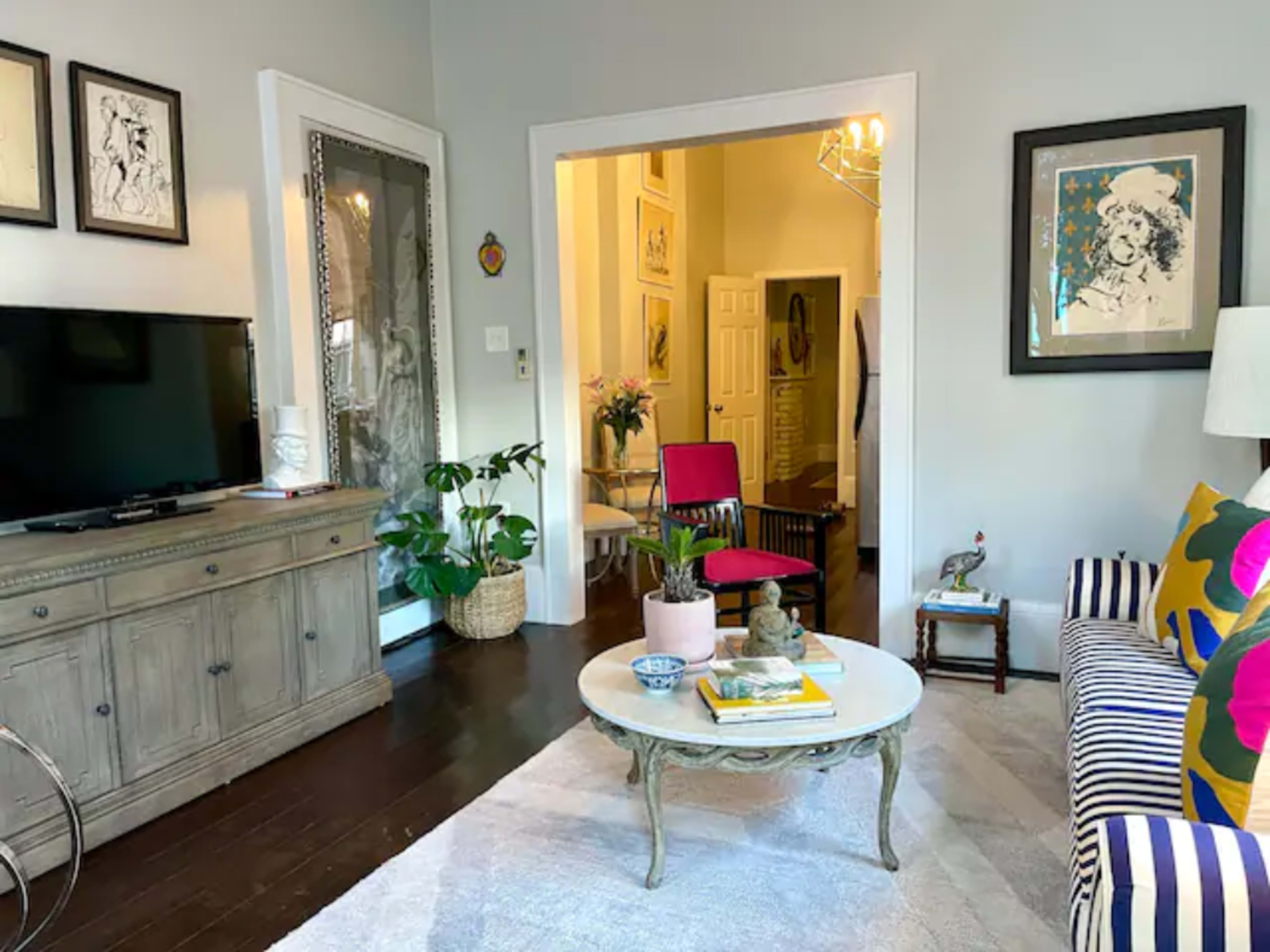 A cozy living room with a striped sofa, a round coffee table, a television, and a doorway leading to a hallway.