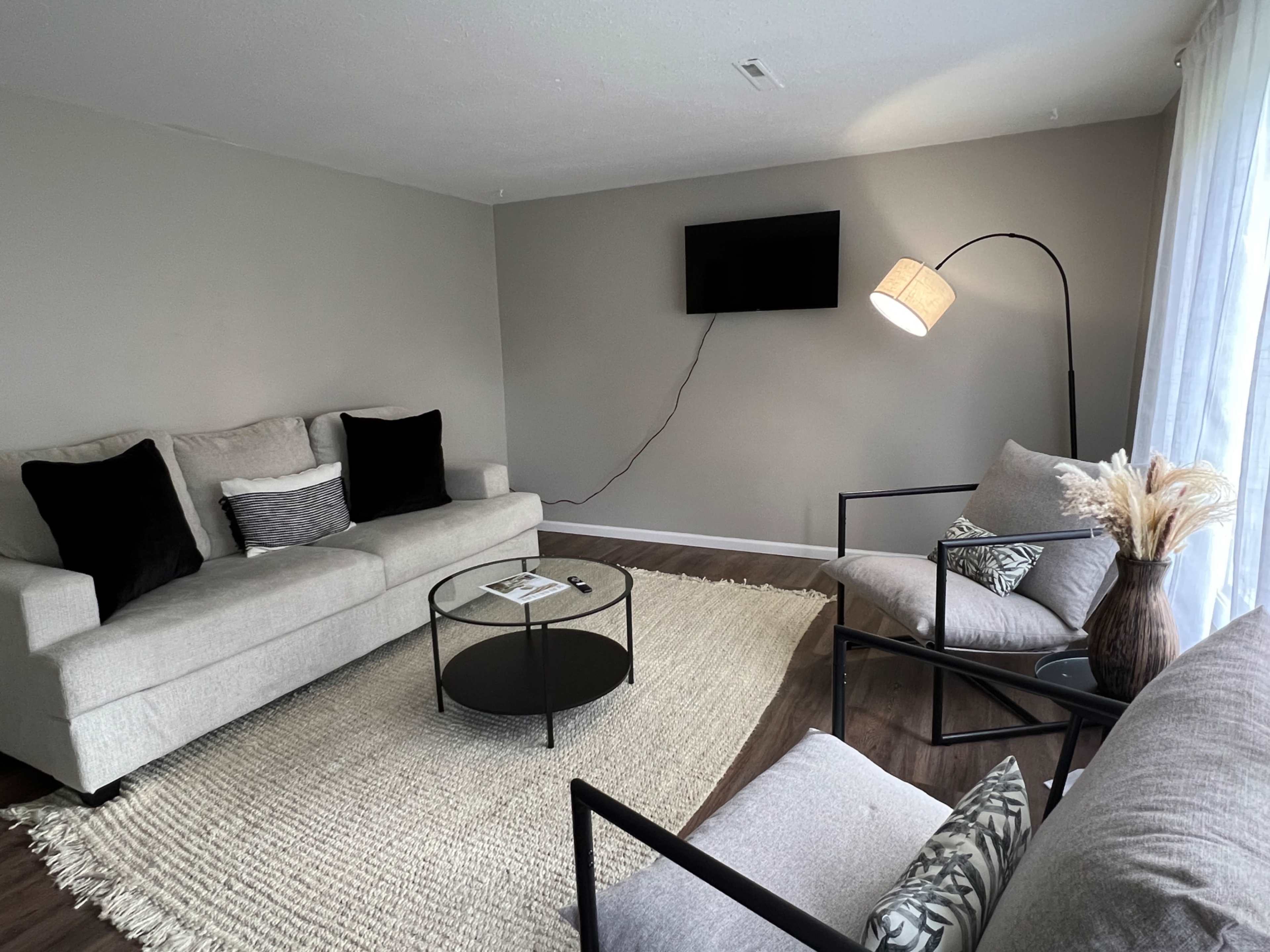 A living room with two sofas, a black coffee table, a floor lamp, and a television mounted on the wall.