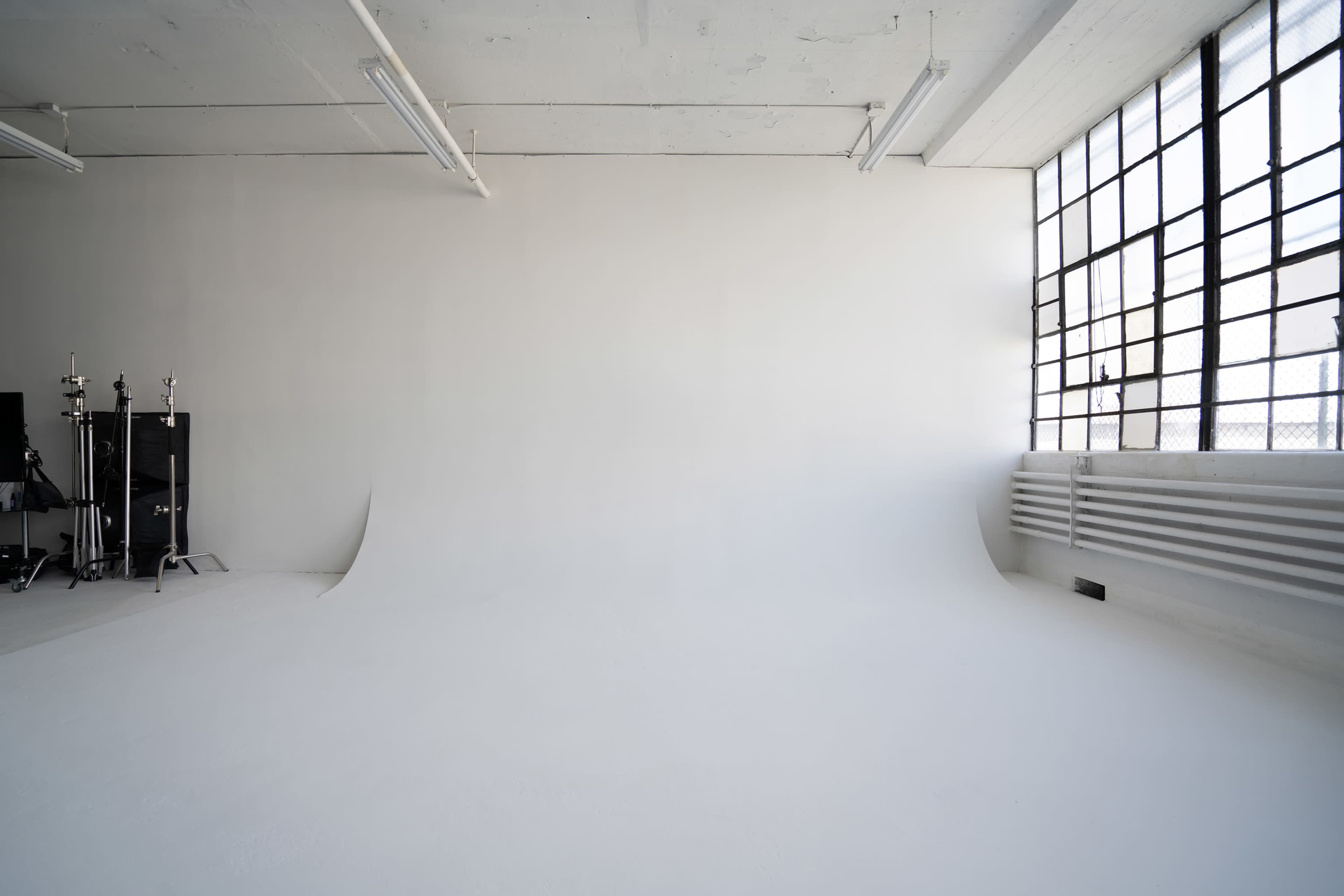 A spacious, empty photography studio with a white backdrop, concrete walls, and large windows.