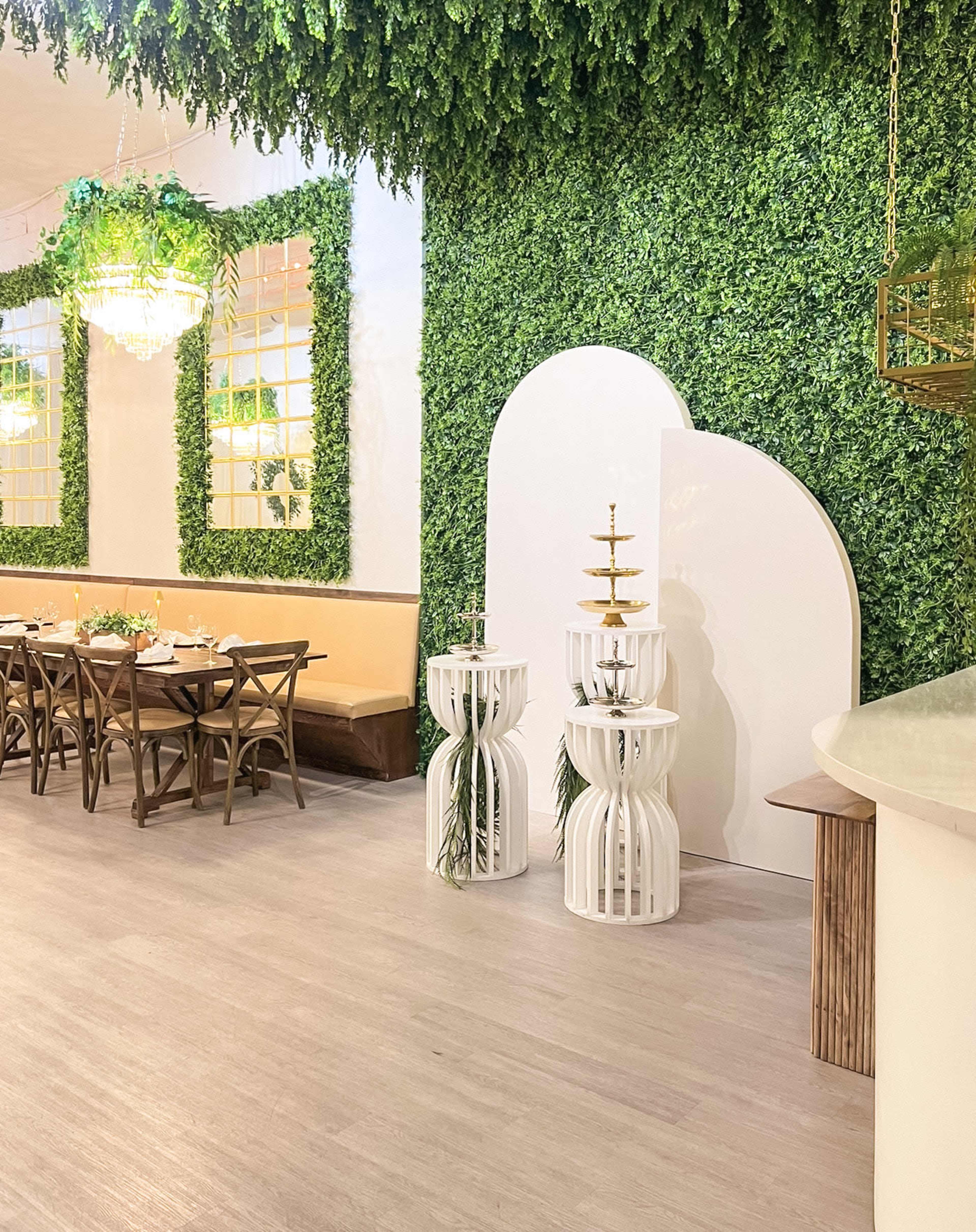 The scene features a modern interior with greenery-covered walls, wooden dining tables, and a unique decorative structure beside a small fountain.