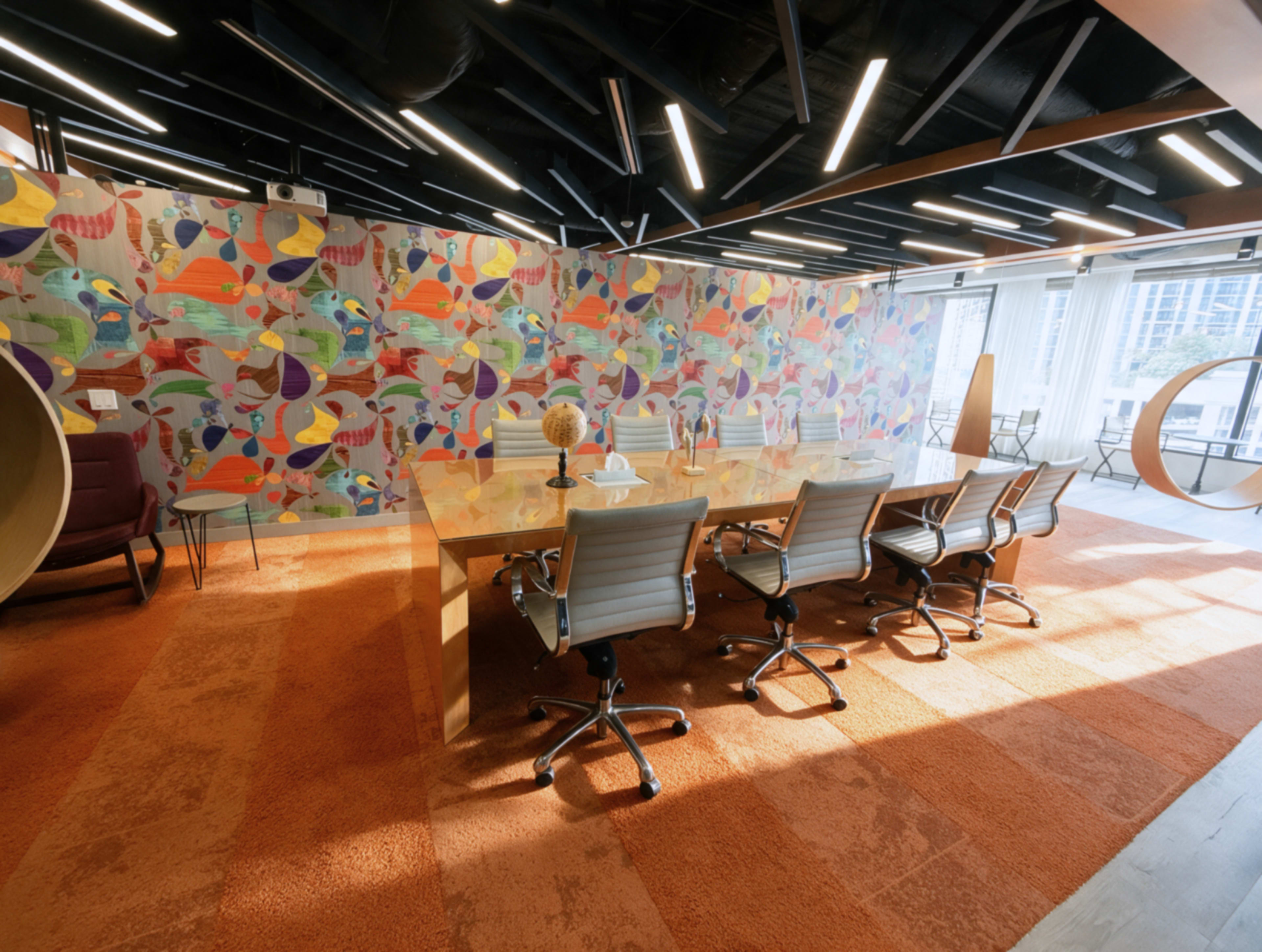 The image shows a modern conference room with a large table surrounded by office chairs, set against a colorful mural on the wall.