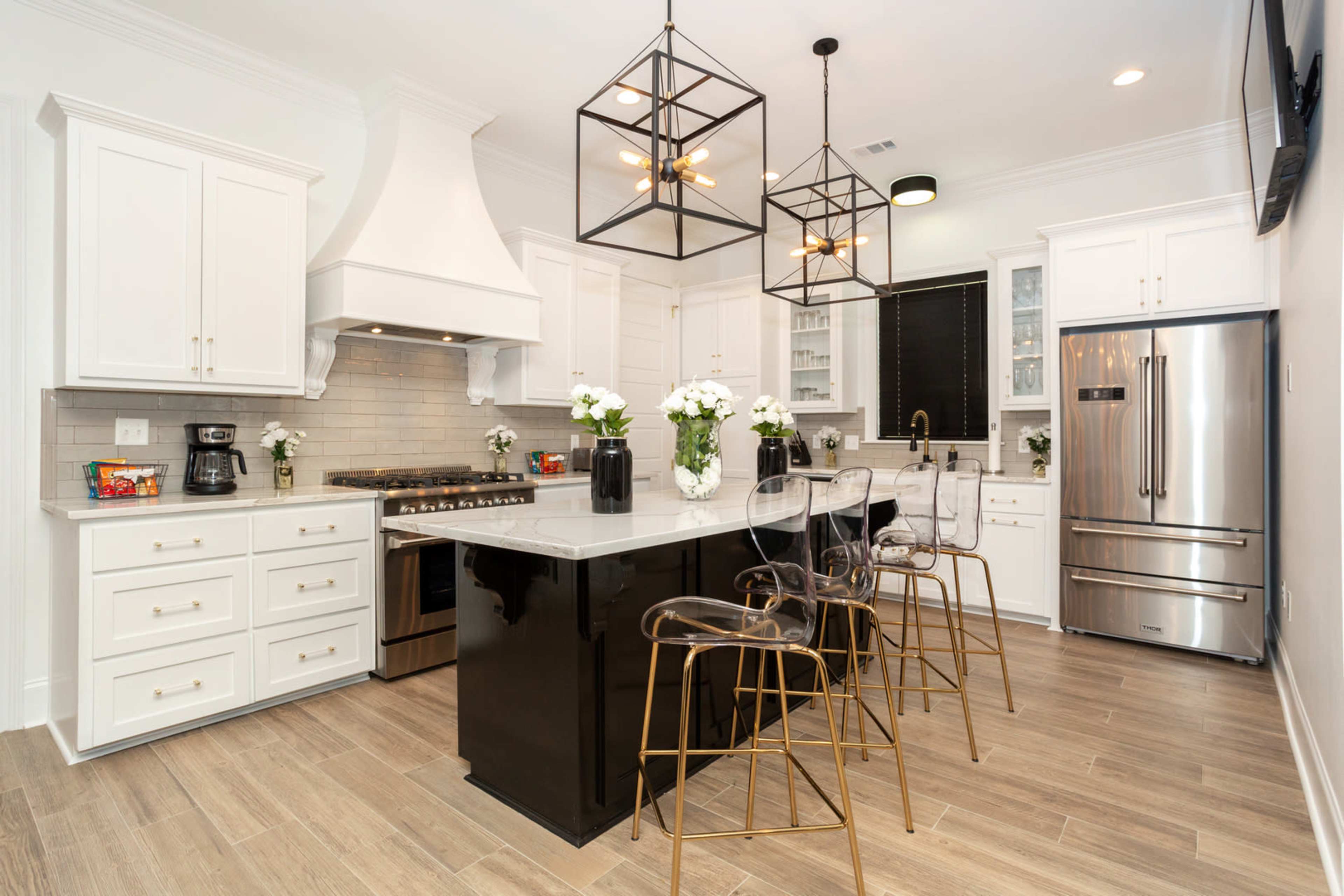 The kitchen features white cabinetry, a large central island with bar seating, stainless steel appliances, and industrial-style light fixtures.