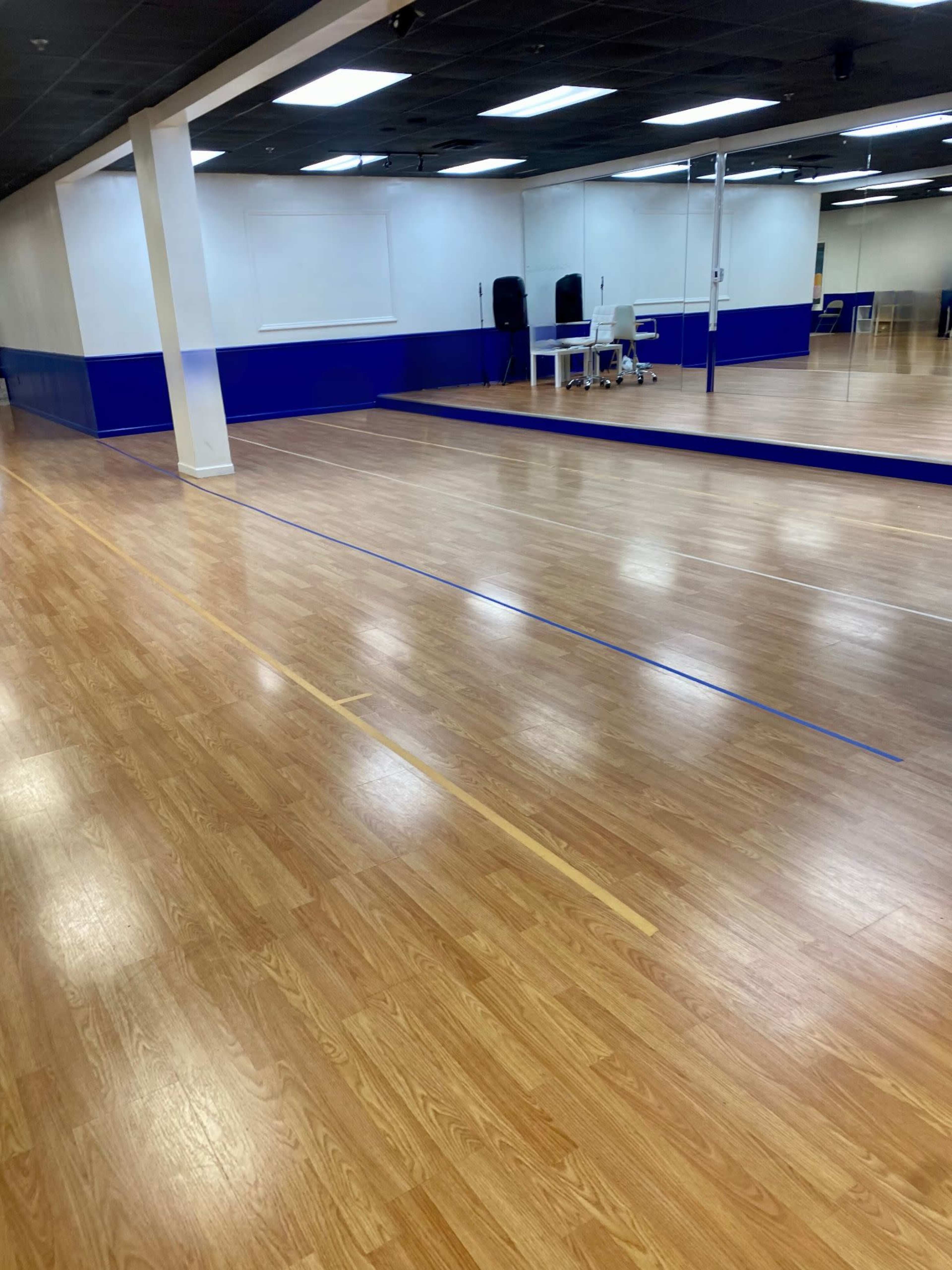 A spacious dance studio with polished wooden floors and a large mirror along one wall.