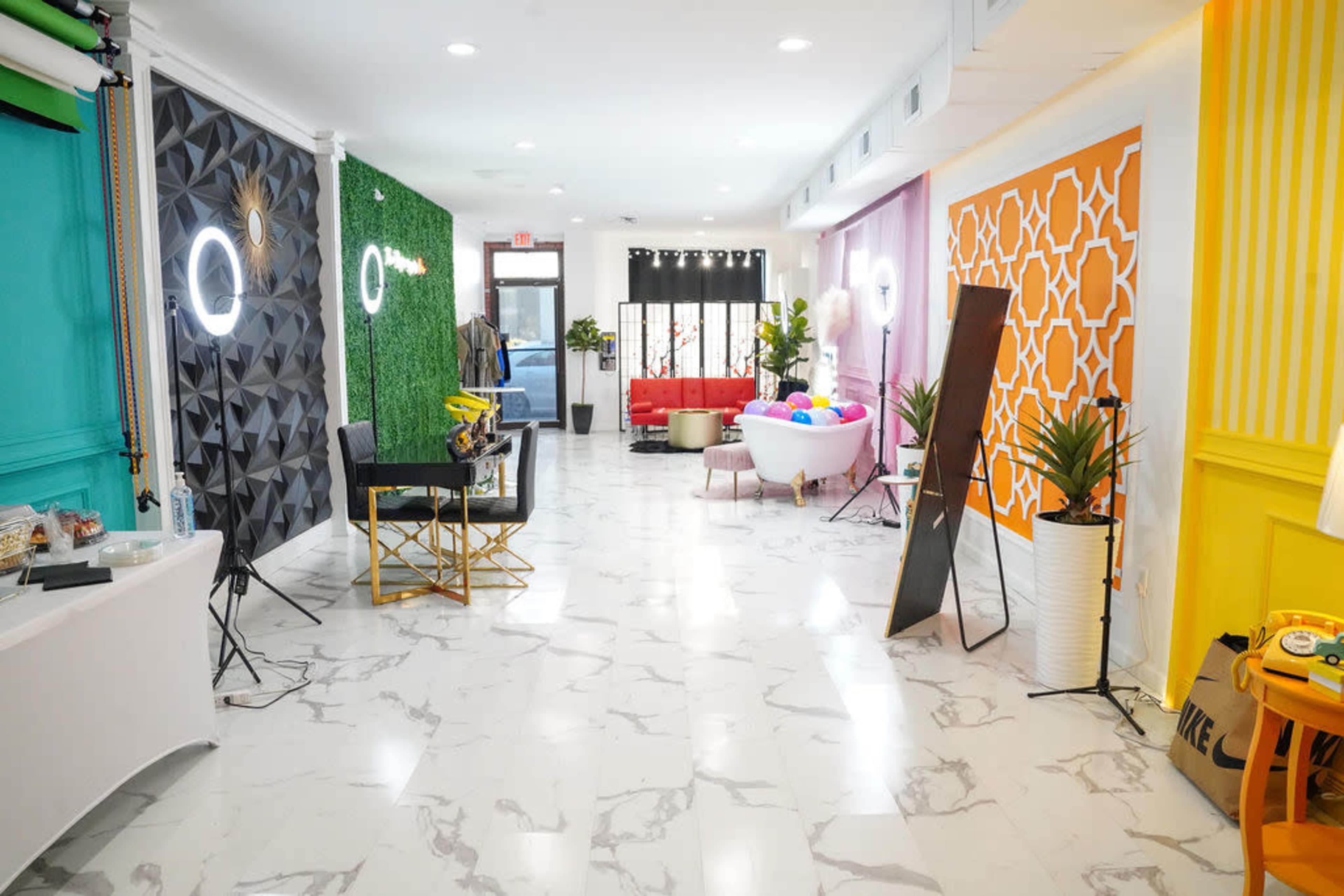 A brightly lit interior space with various colorful walls, modern furniture, and a mix of decorative elements, including plants and lighting setups.