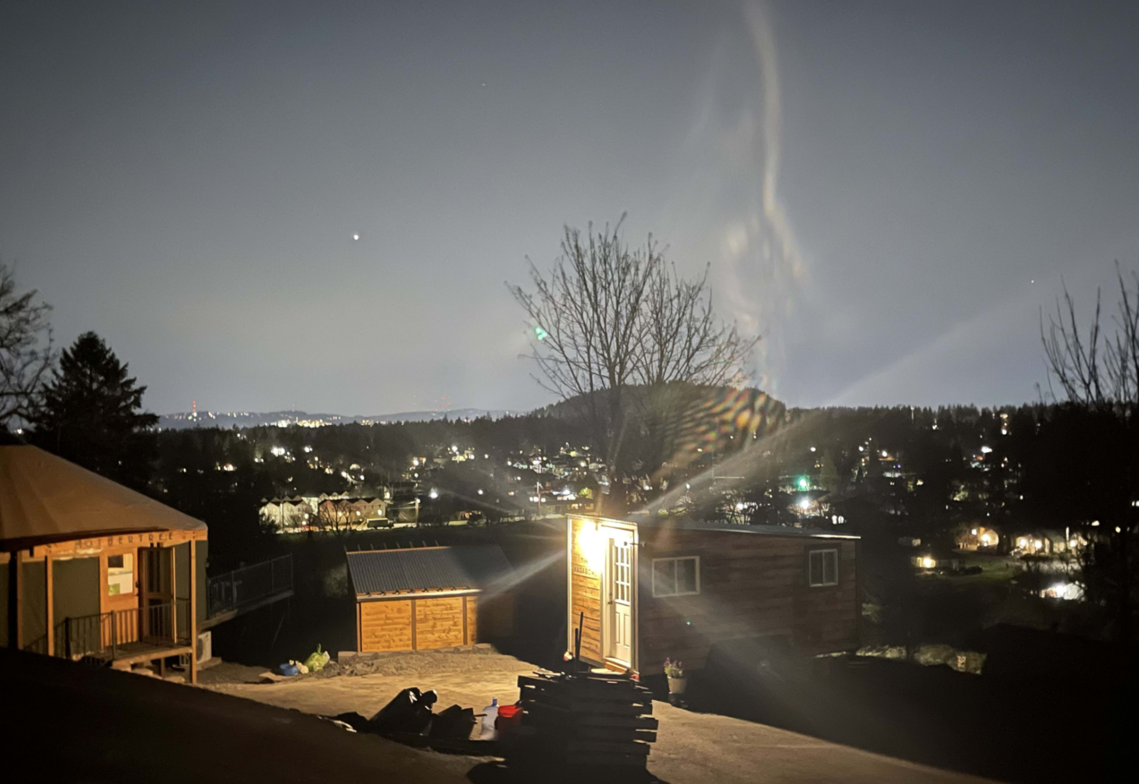 A brightly lit cabin stands on a hillside overlooking a city illuminated by night lights.