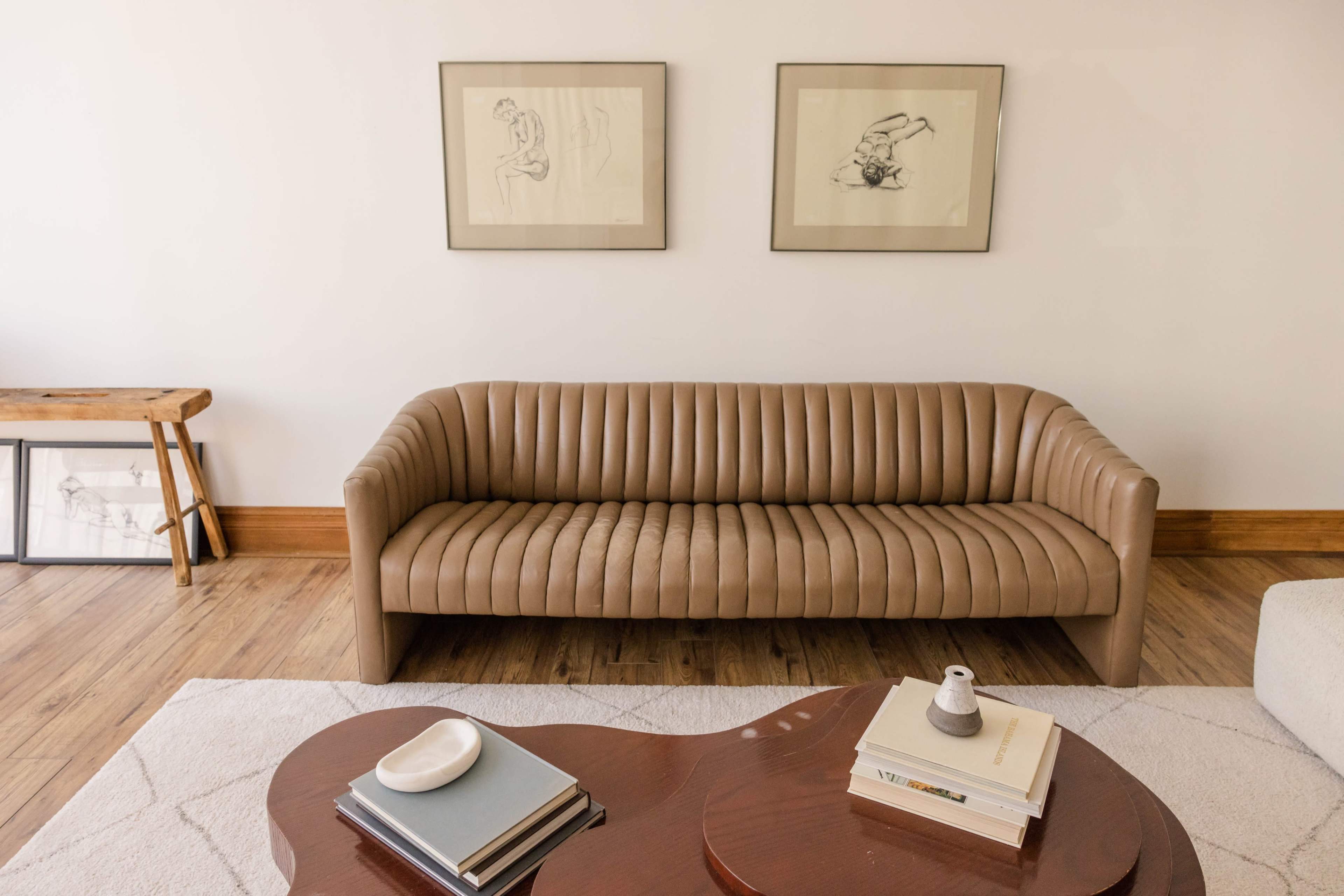 A light brown ribbed sofa is positioned in front of a wooden coffee table, with two framed artworks hanging on the wall above.