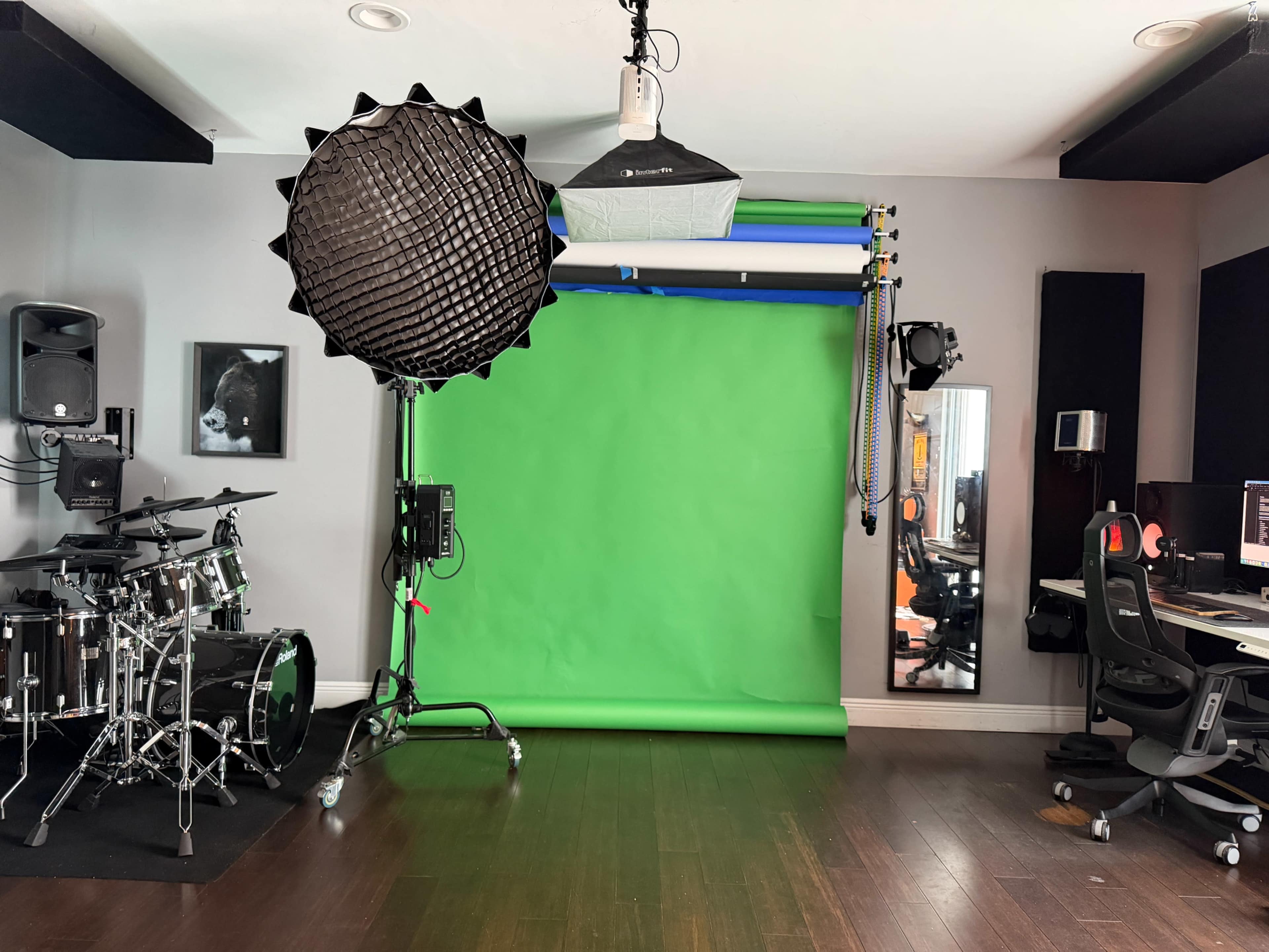 The image shows a studio setup featuring a green screen, lighting equipment, a drum kit, and workstations with computers.