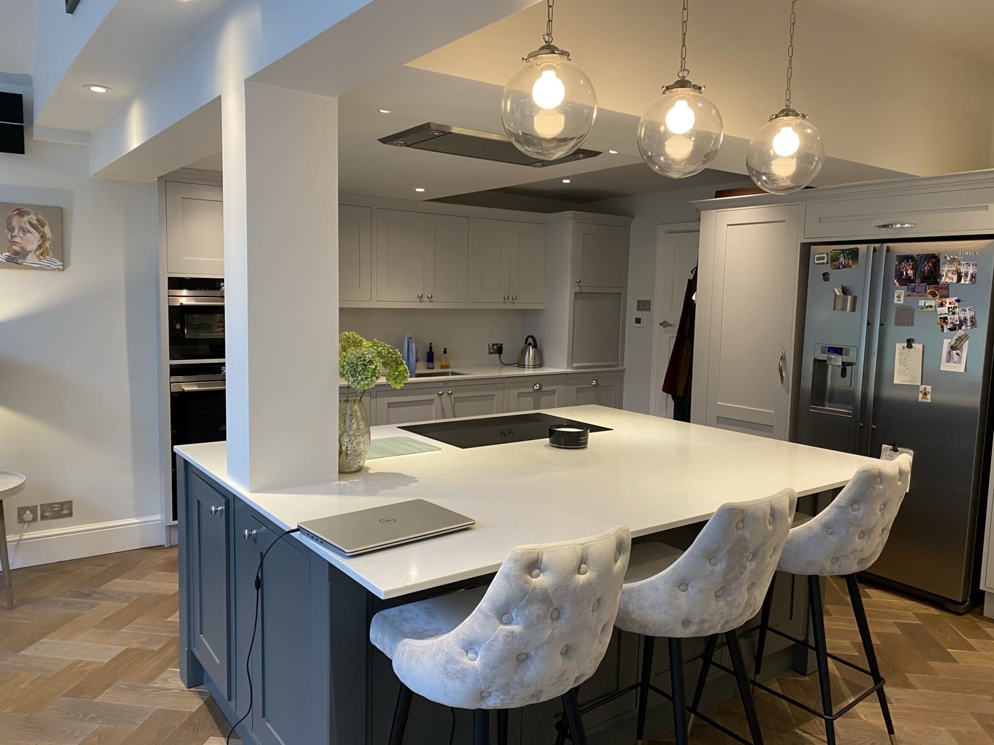 A modern kitchen with a large island, featuring three upholstered bar stools, pendant lights, and stainless steel appliances.