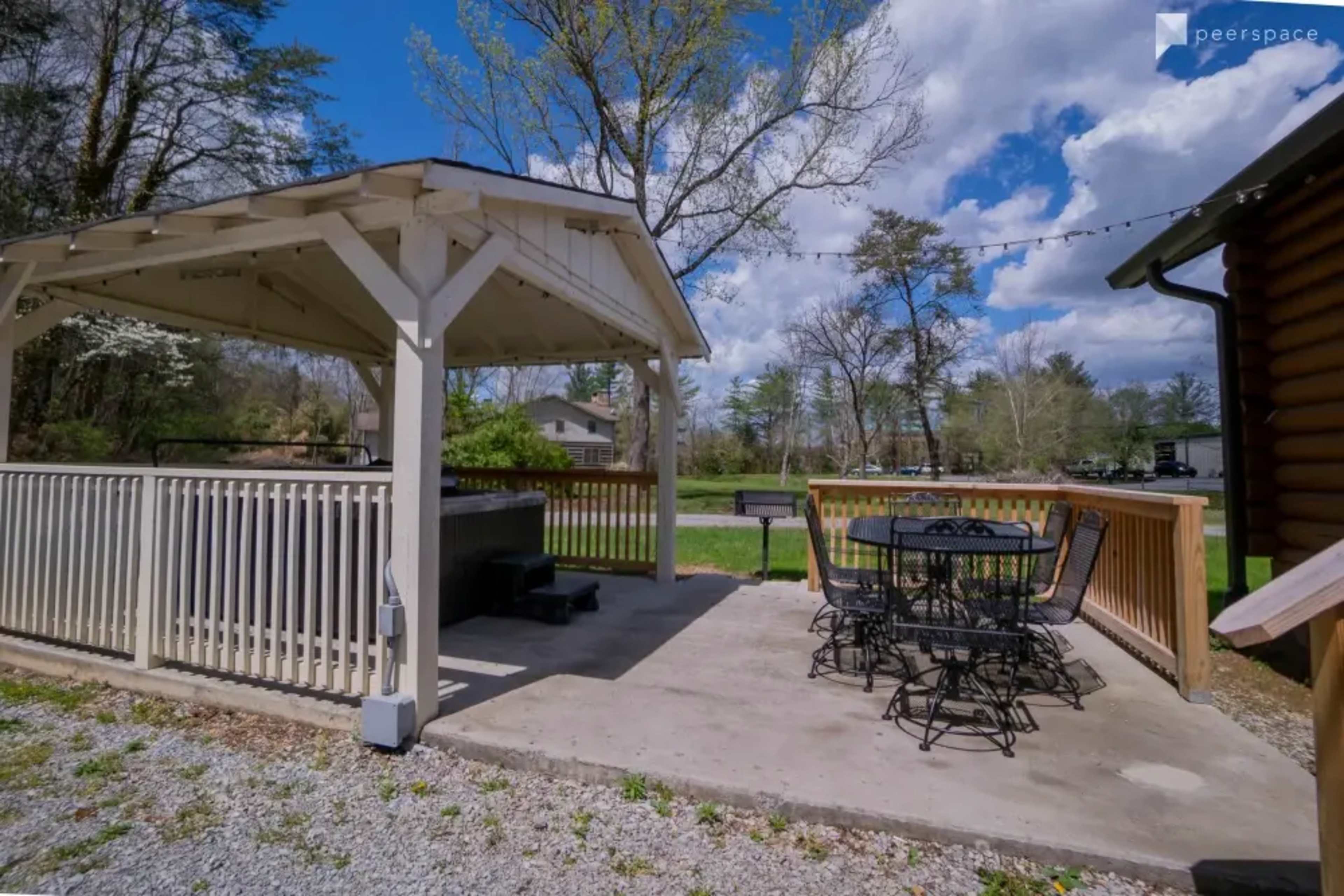 A gazebo with a seating area and a hot tub on a concrete patio, surrounded by trees and grass.