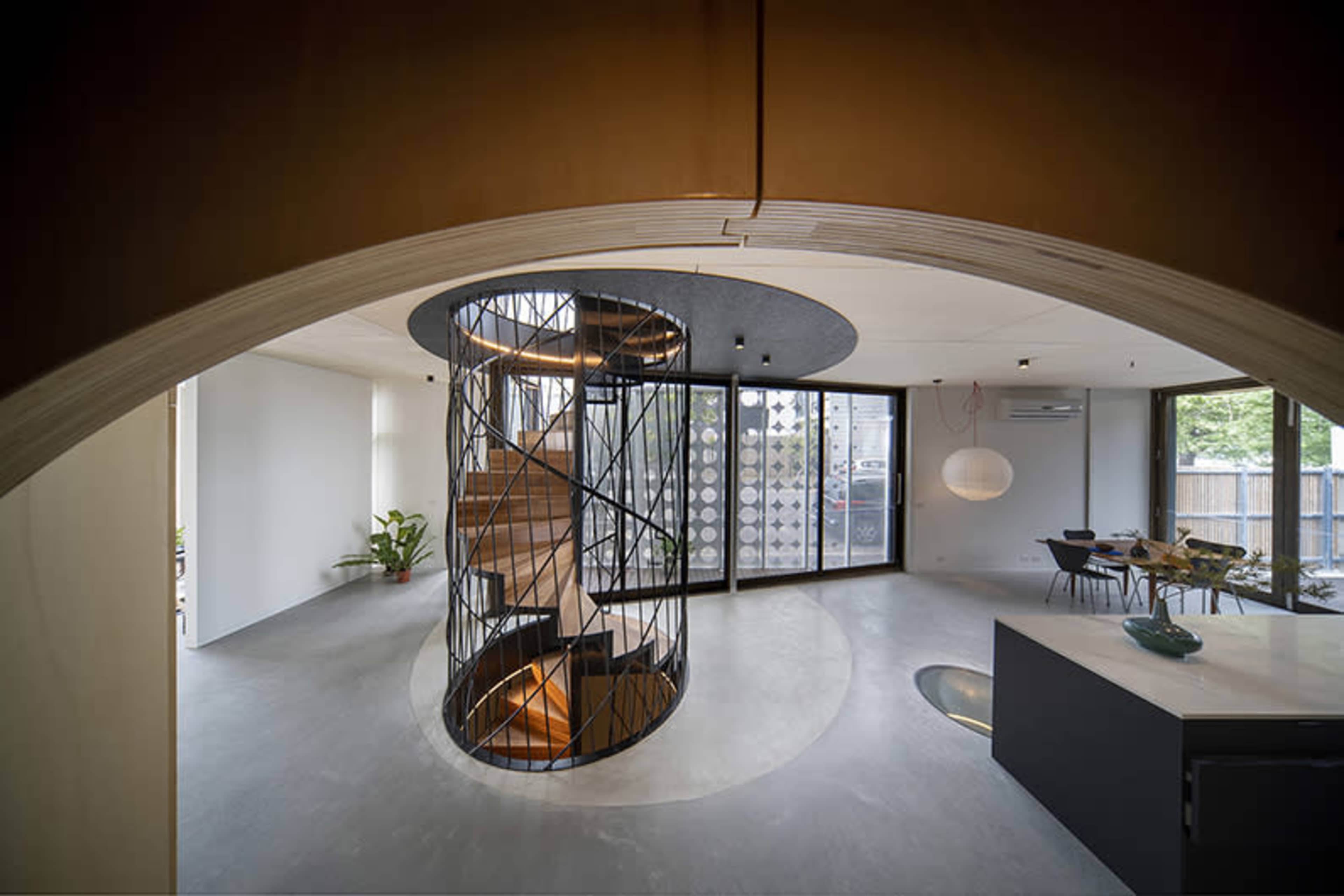 A modern interior space with a spiral staircase at its center, surrounded by large windows and minimalist furniture.
