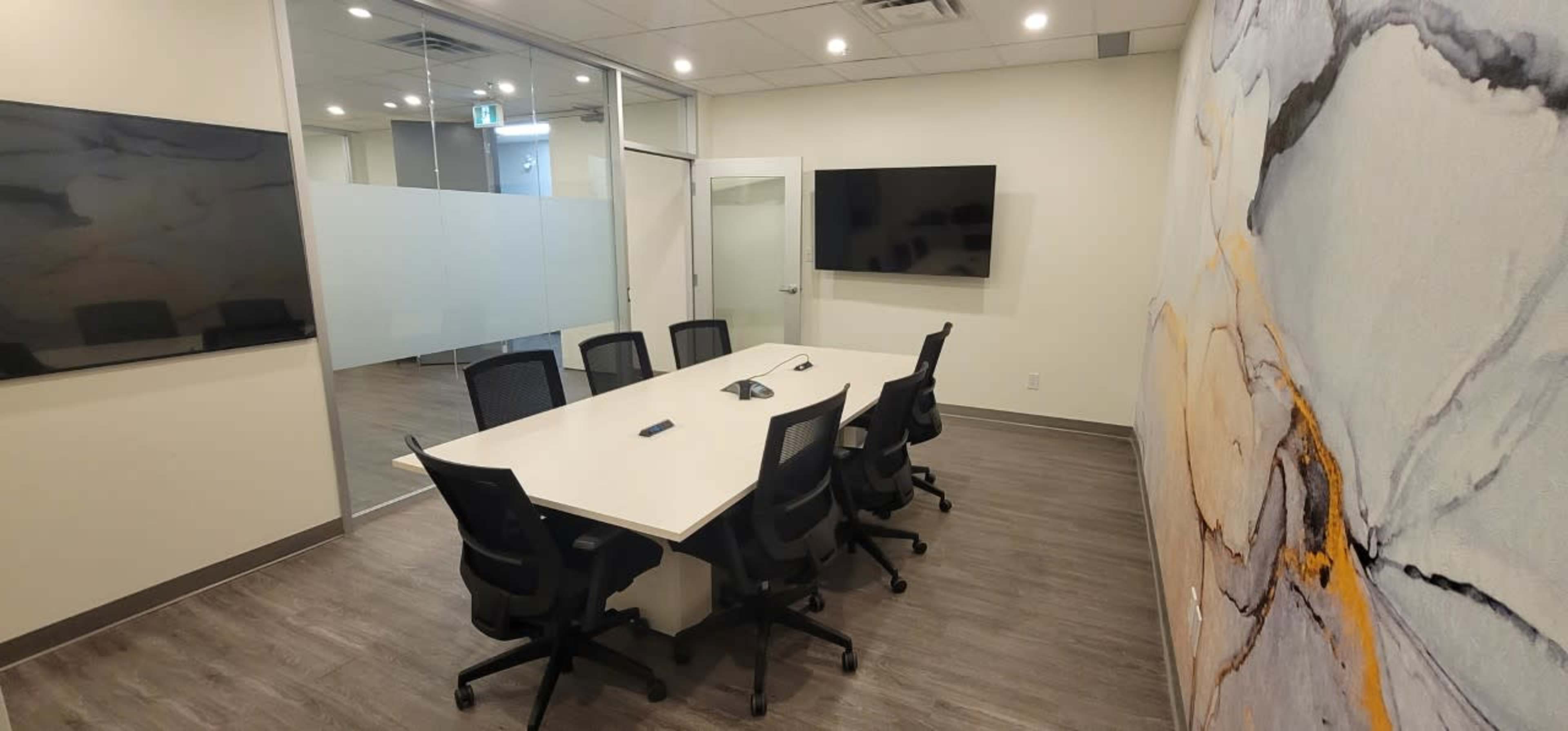 A modern conference room with a long table, several black chairs, and multiple wall-mounted screens.
