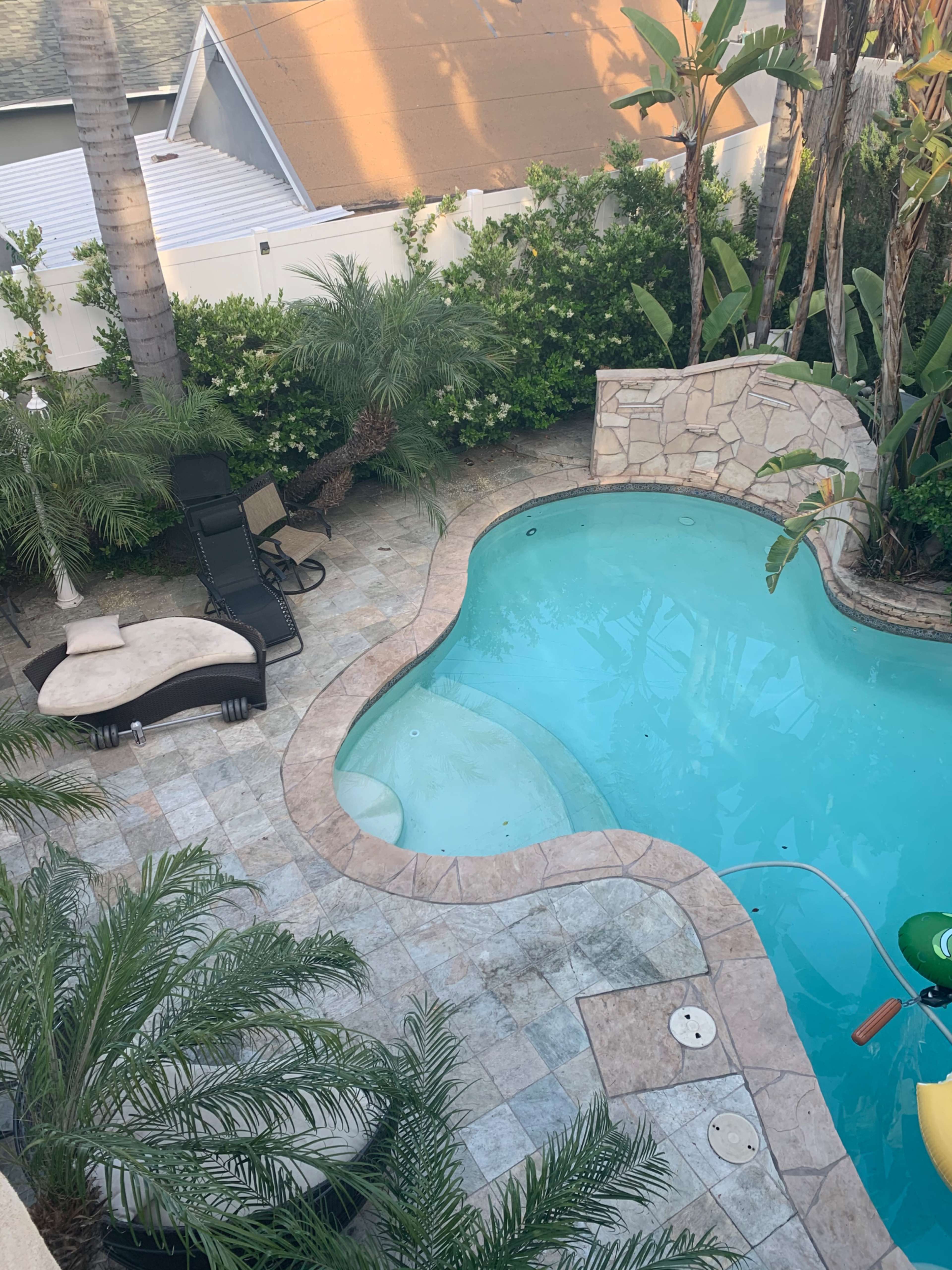 An aerial view of a landscaped pool area surrounded by palm trees and stone paving.