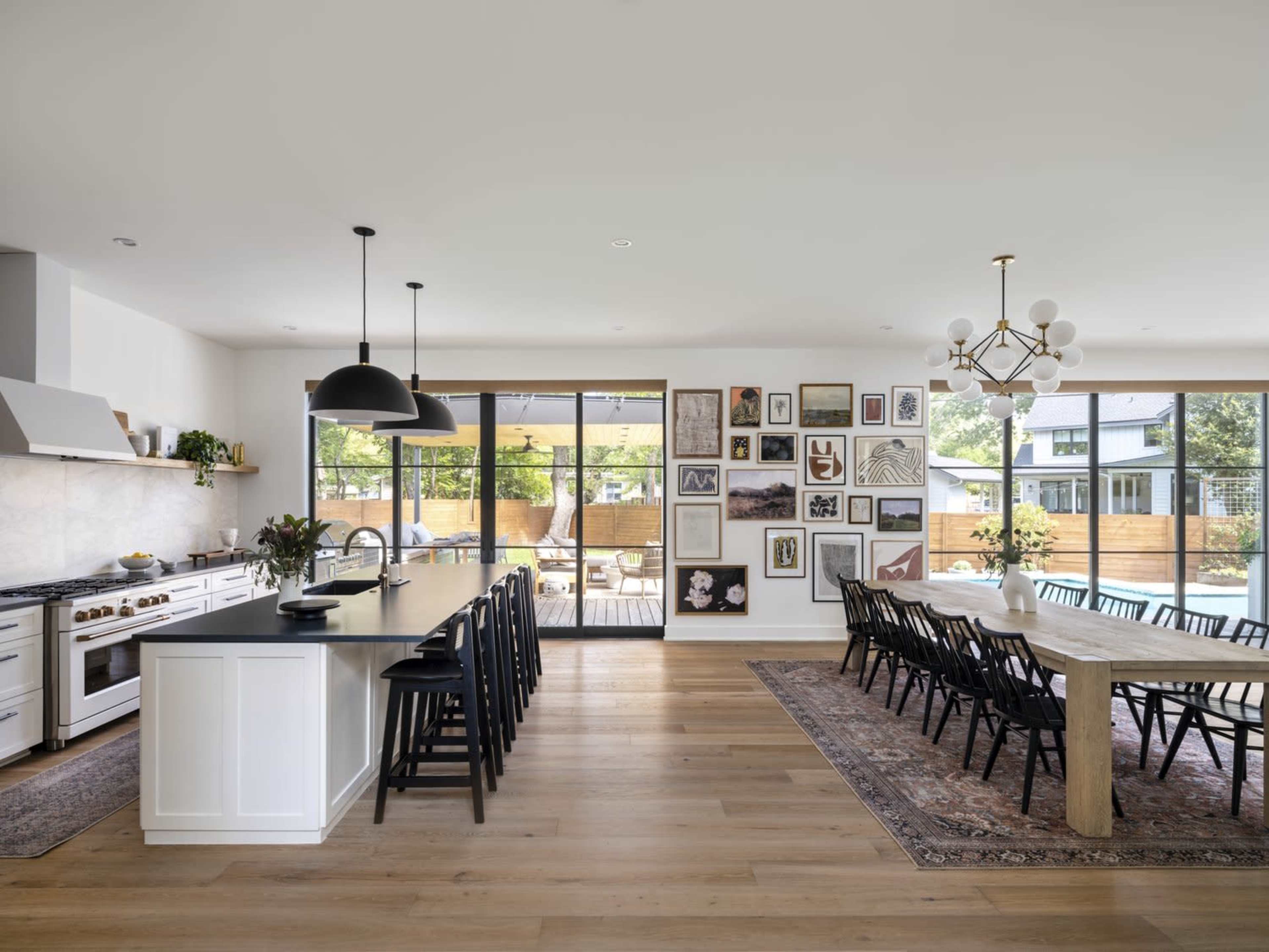 A modern kitchen features a large island with bar seating and a dining area adjacent to a wall displaying a collection of framed artwork.