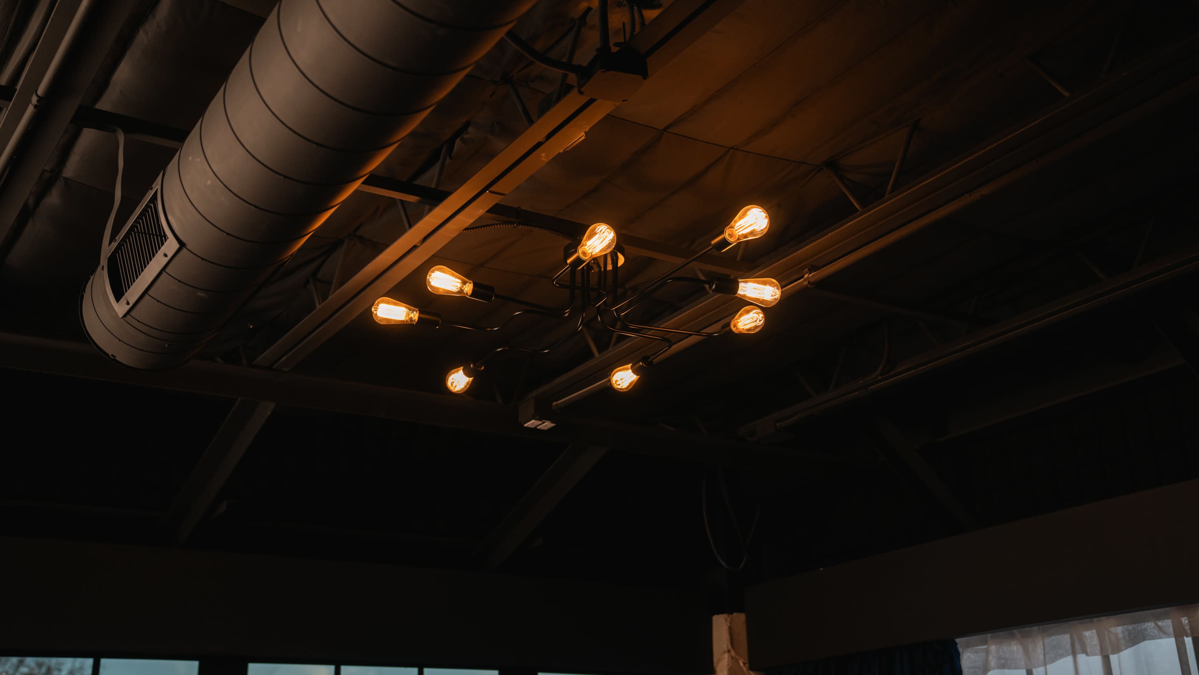 The image shows a modern industrial-style ceiling light fixture with multiple bulbs illuminating a dark room.