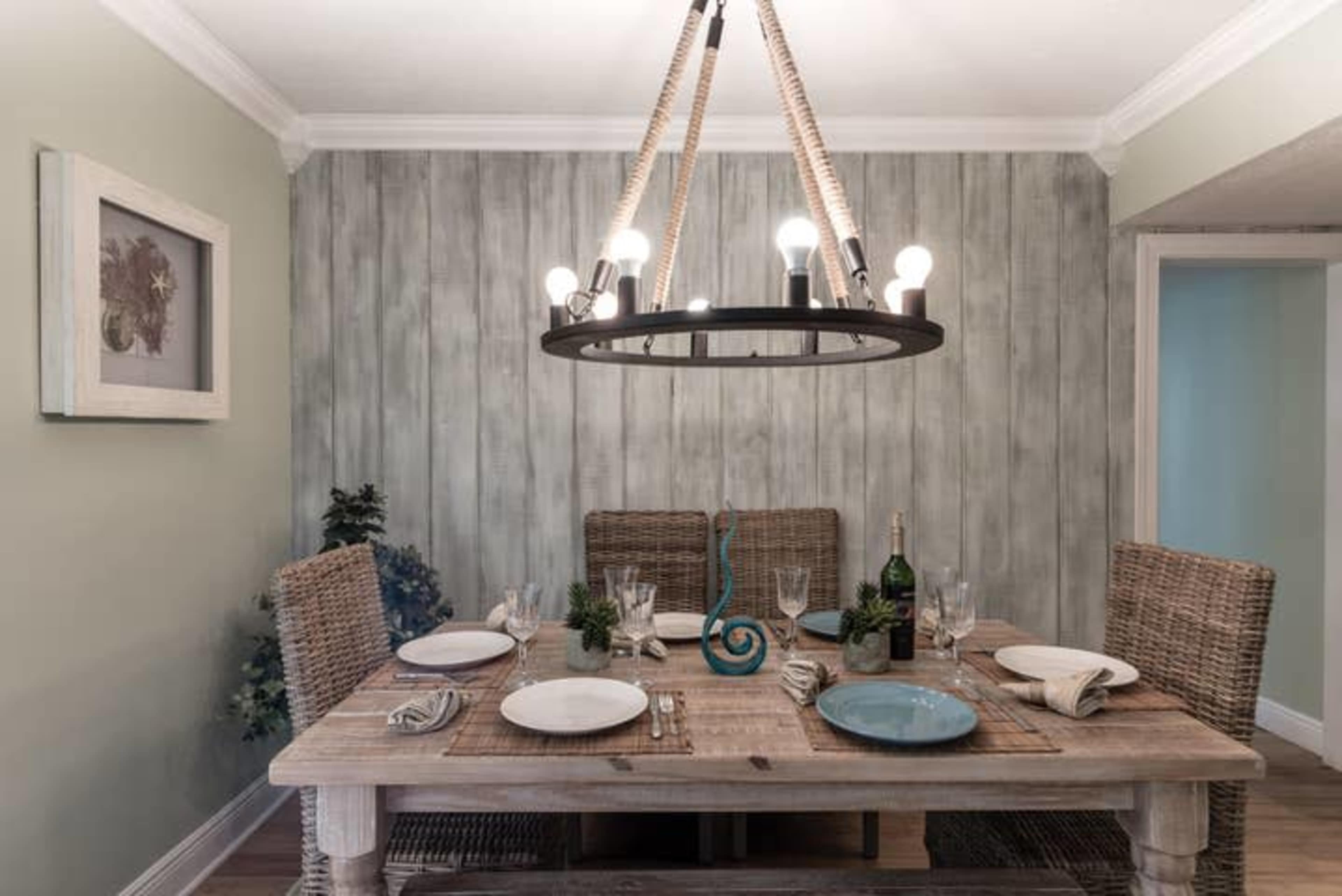 A dining room features a wooden table set with dinnerware and a large overhead chandelier.