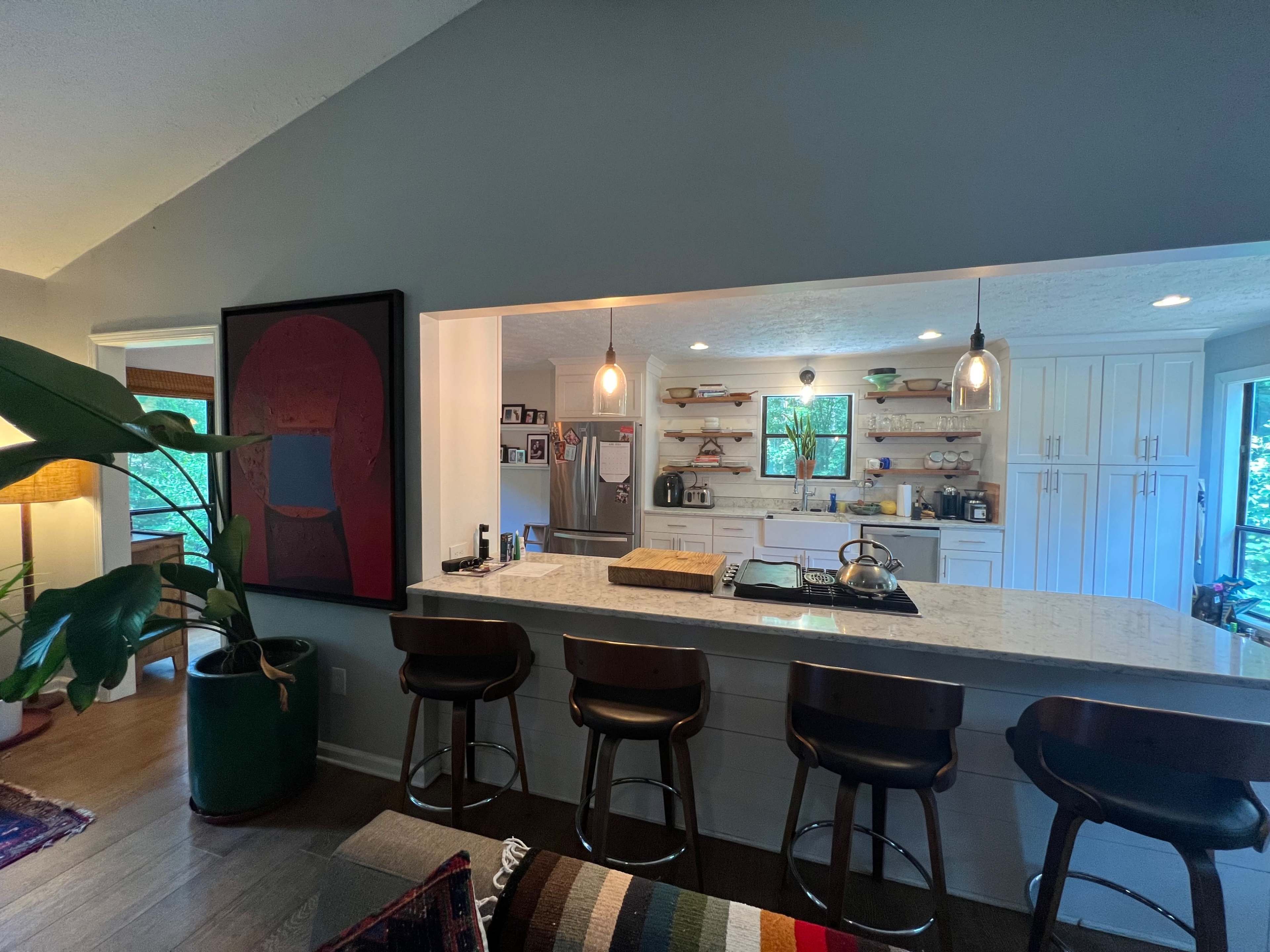The image shows a modern kitchen with a large bar area featuring several stools and an open layout that connects to a living space.