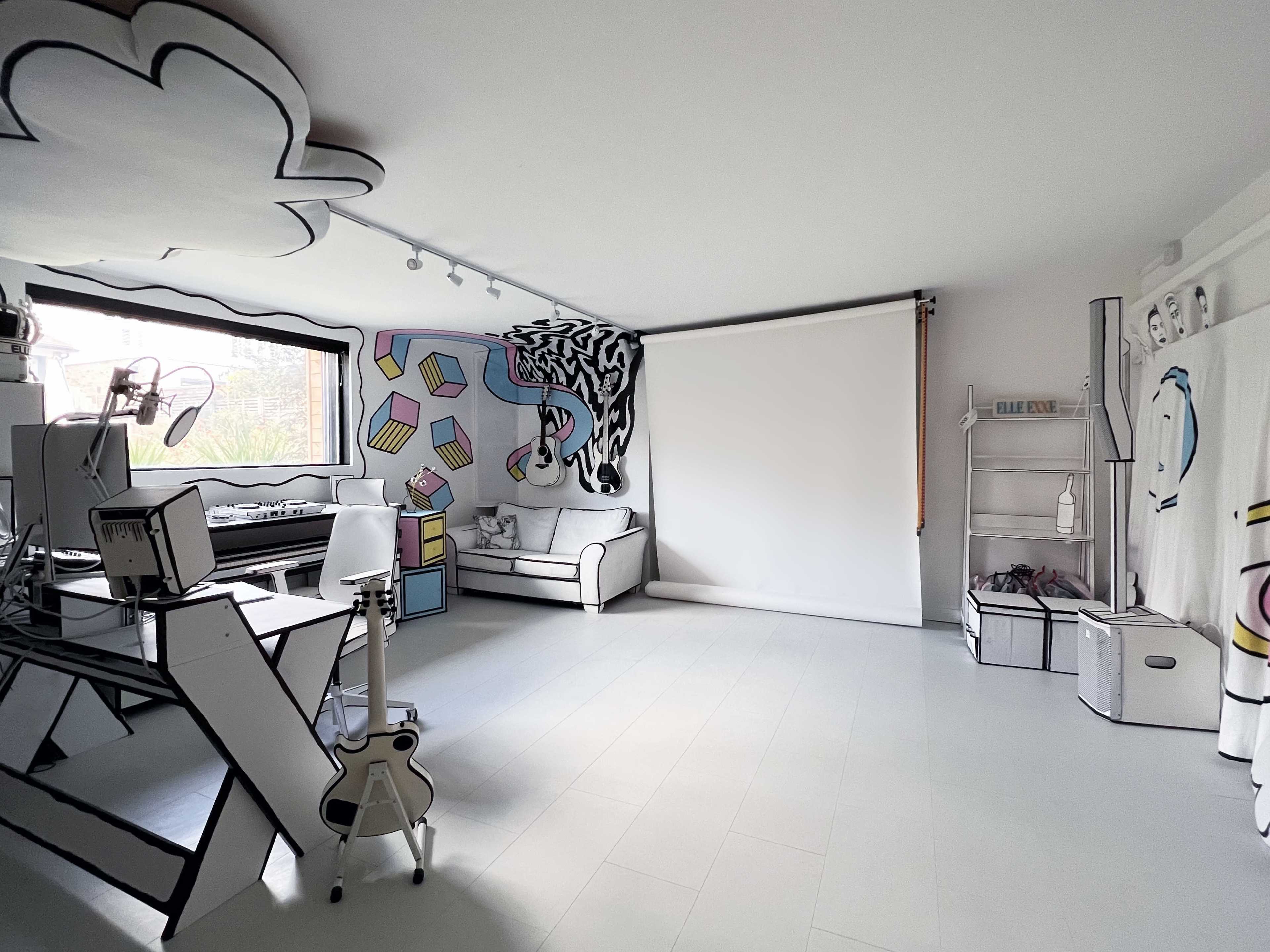 A minimalist room with white walls and furniture, featuring black and white line art drawn on the walls, a projector screen, and various items arranged neatly.