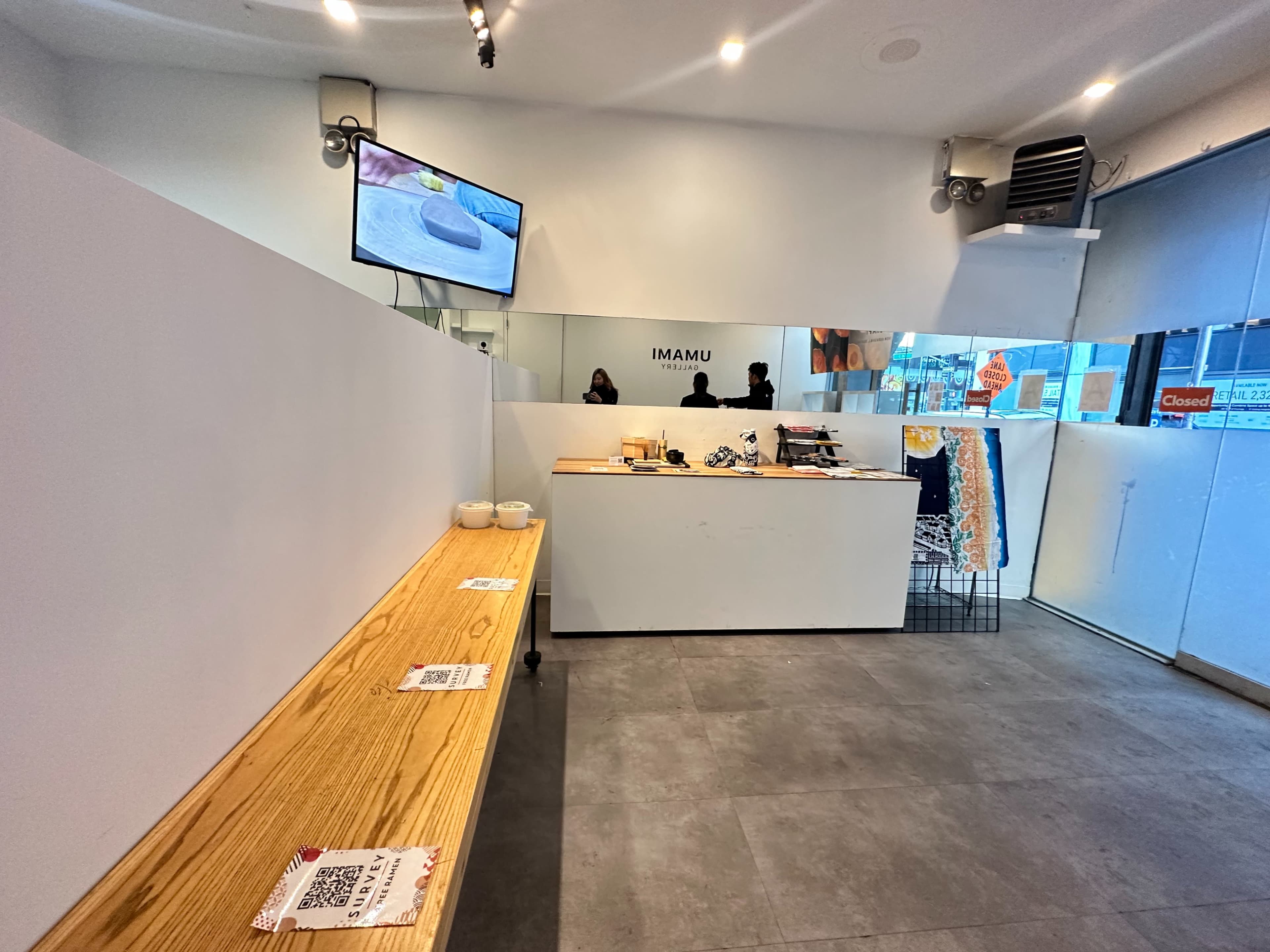 A minimalist interior of a café with a wooden bench, a service counter, and a television mounted on the wall.