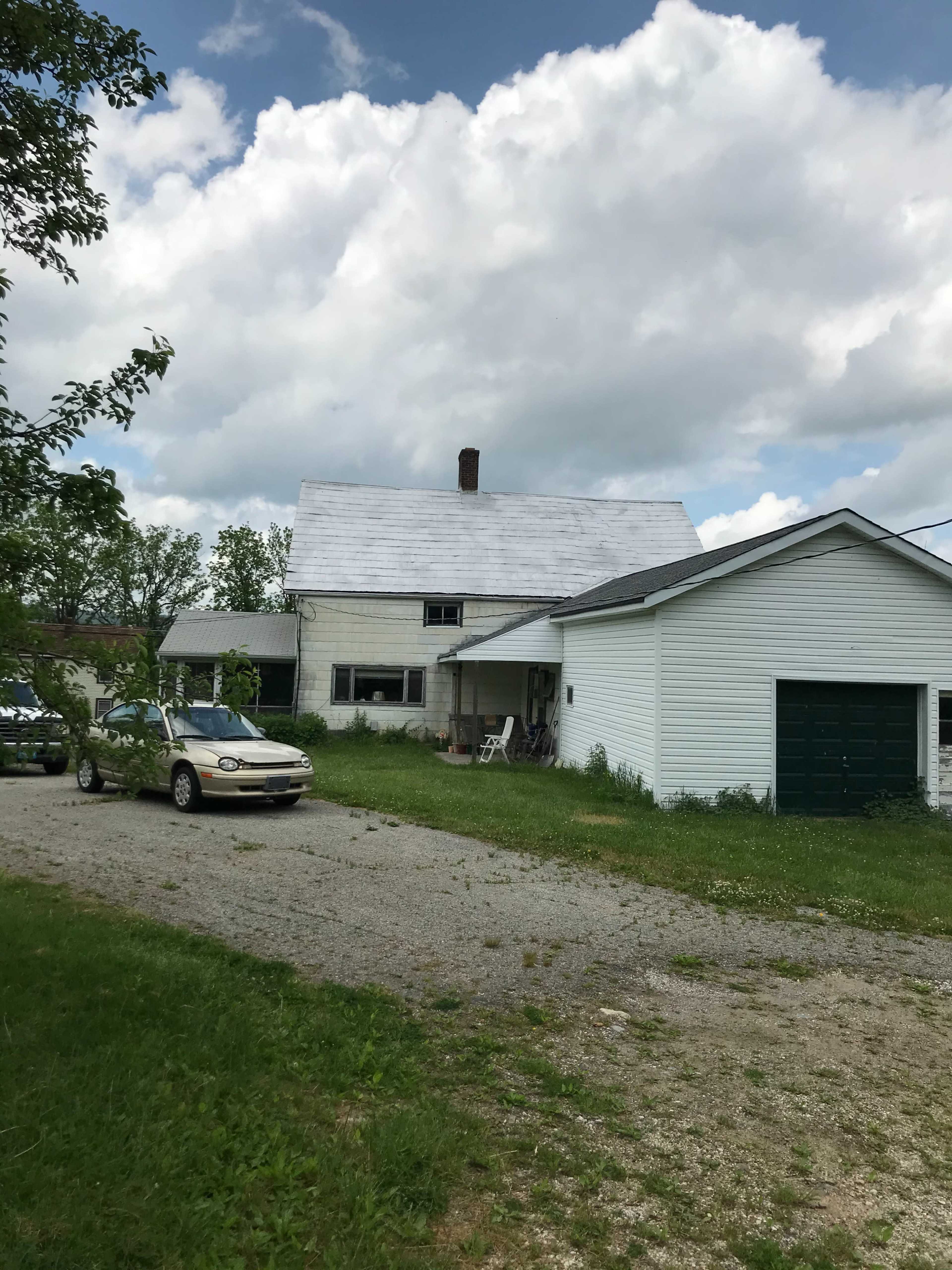 A two-story white house with a gravel driveway and a nearby garage sits under a partly cloudy sky.