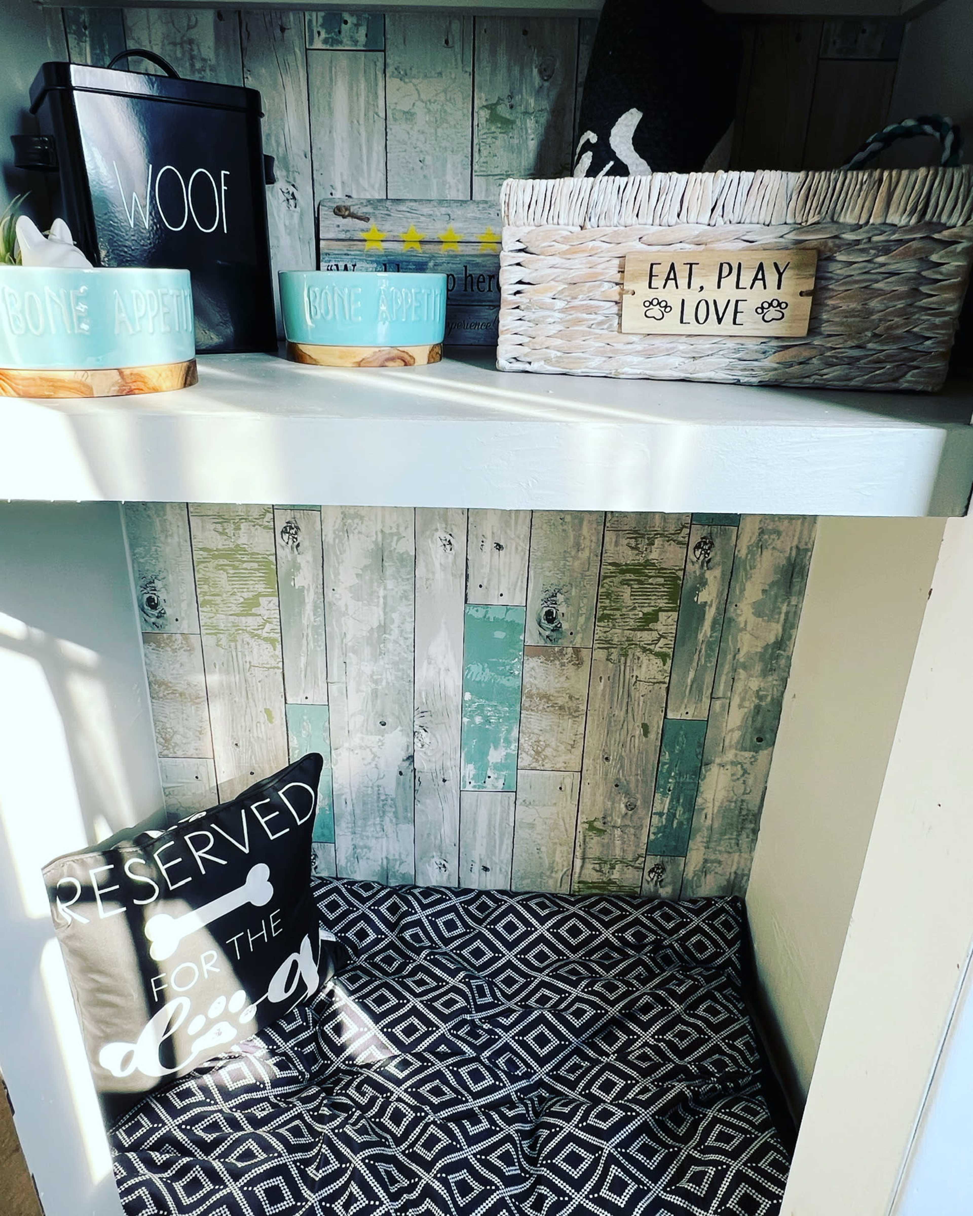 A pet corner with decorative containers, a cushion, and a sign on a shelf, all arranged in a cozy space.