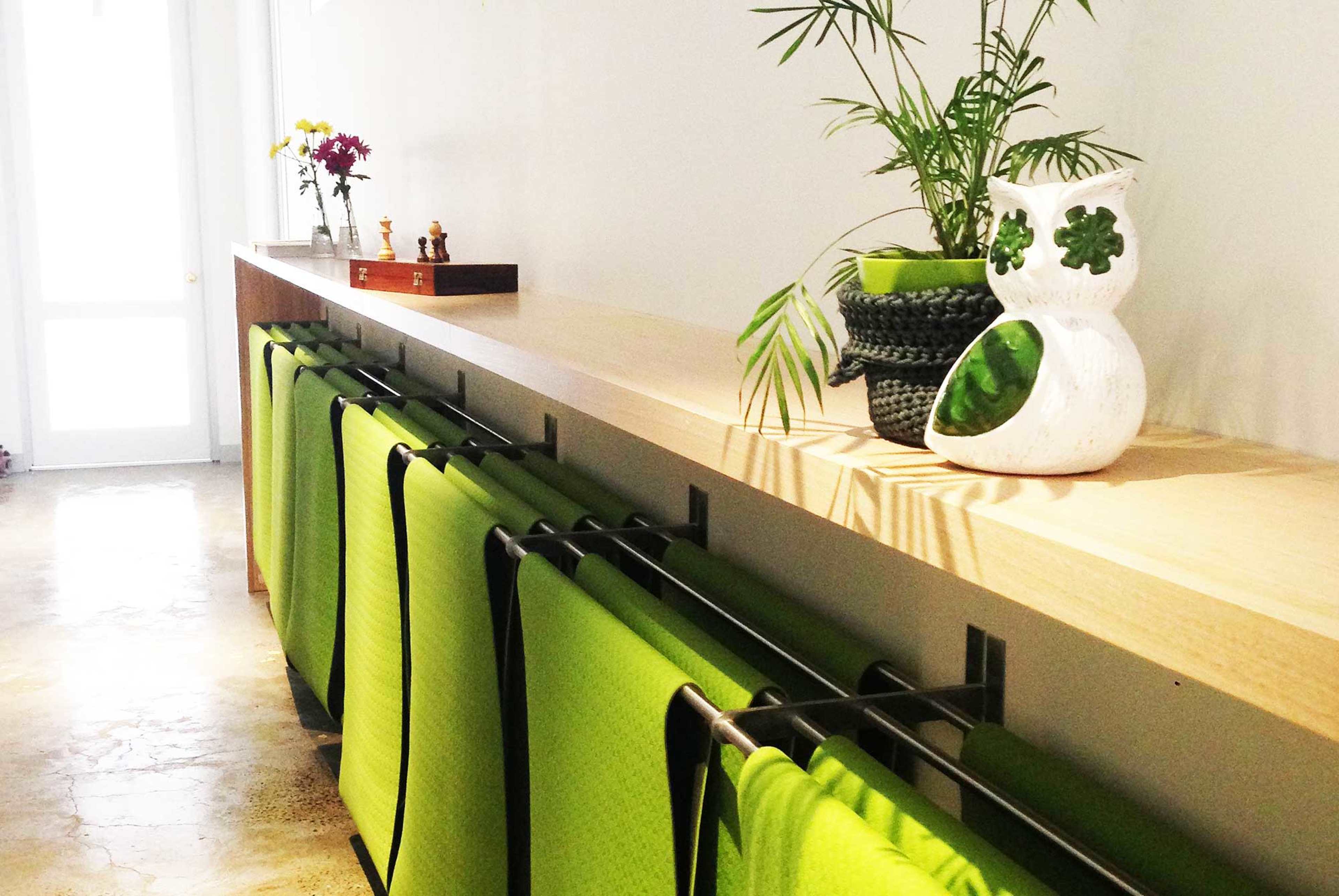 A long wooden shelf holds several green yoga mats and a decorative plant, with a small bouquet of flowers and other items arranged on top.