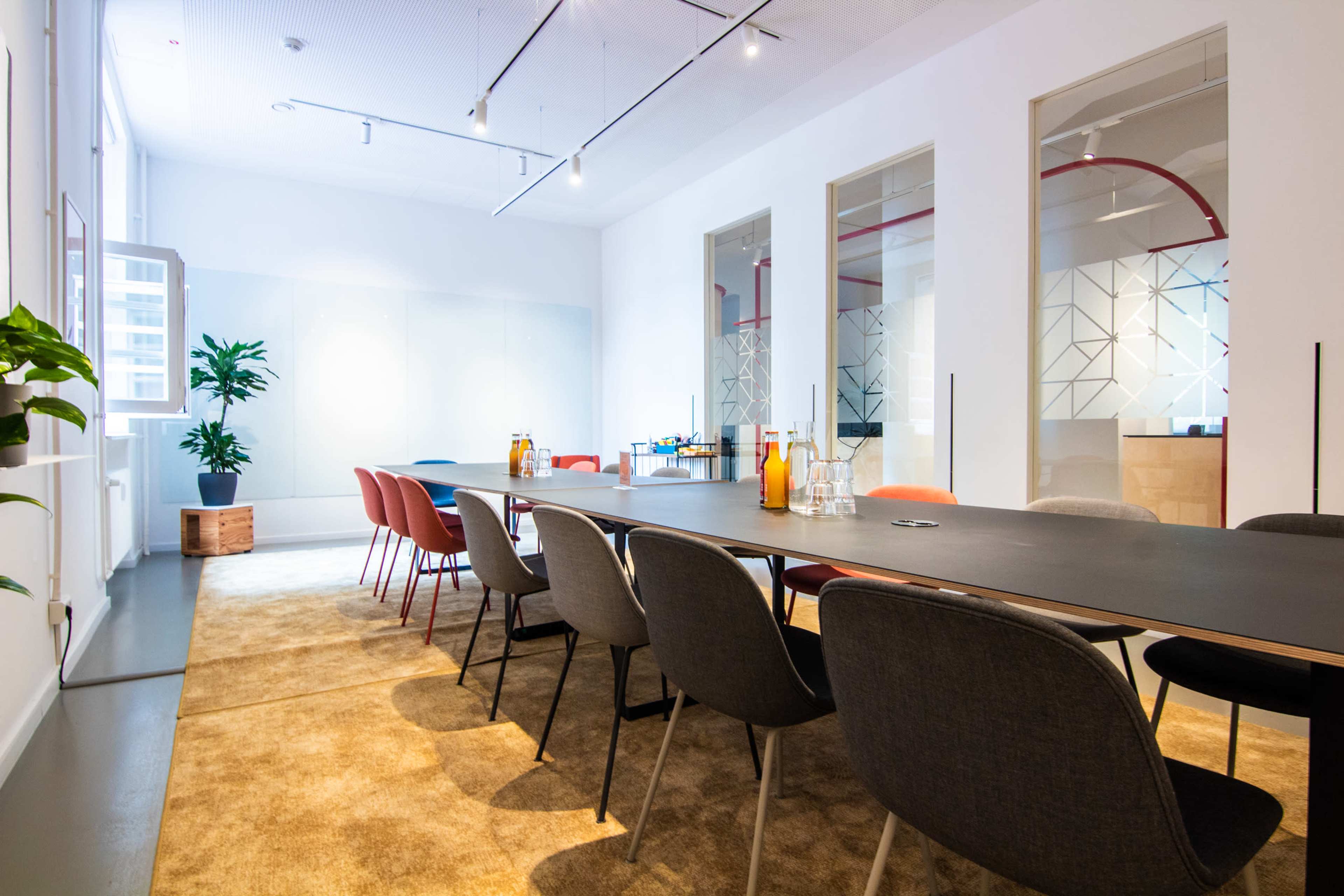A modern meeting room features a long table surrounded by chairs and large windows allowing natural light.