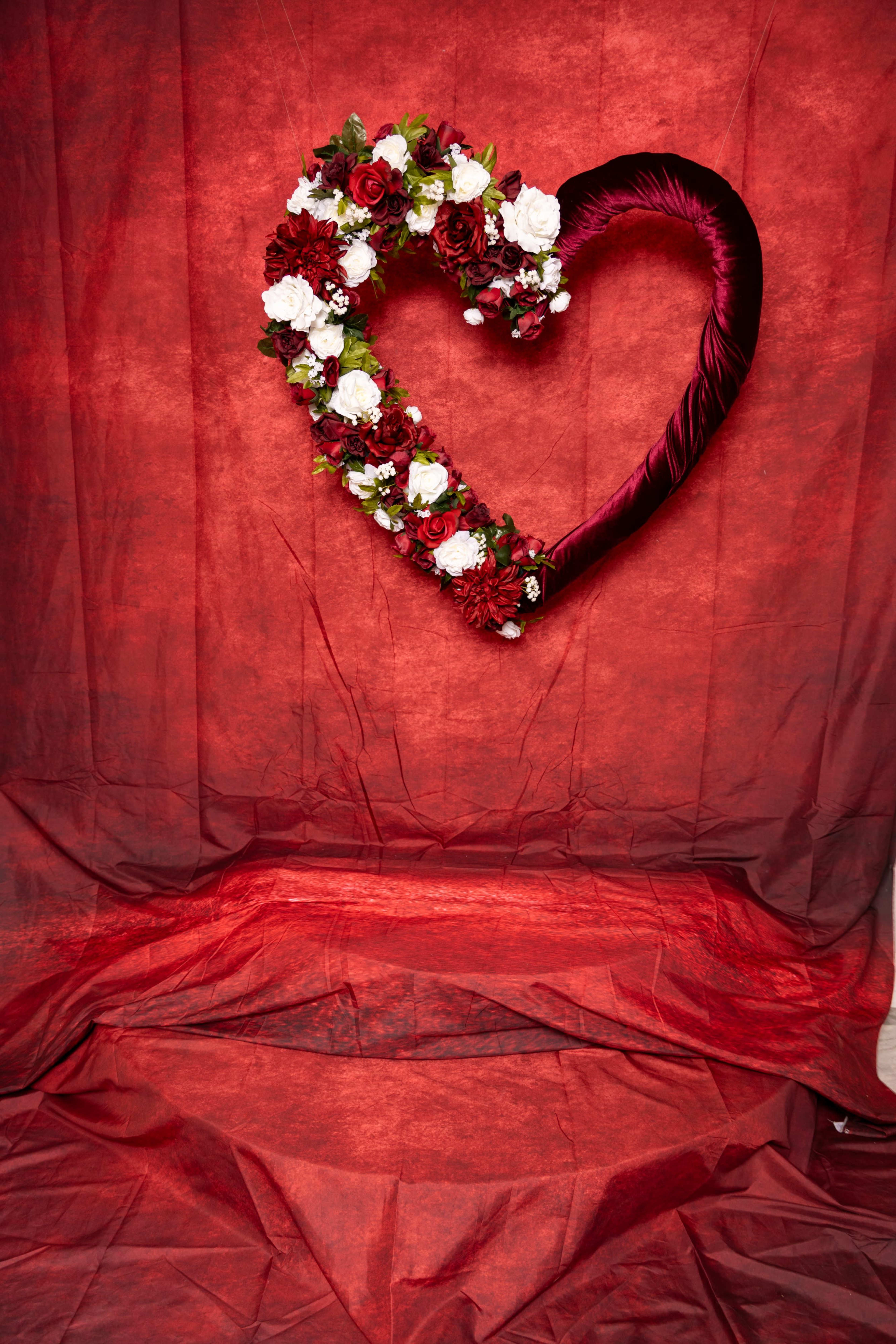 A floral heart-shaped wreath is displayed against a textured red background.