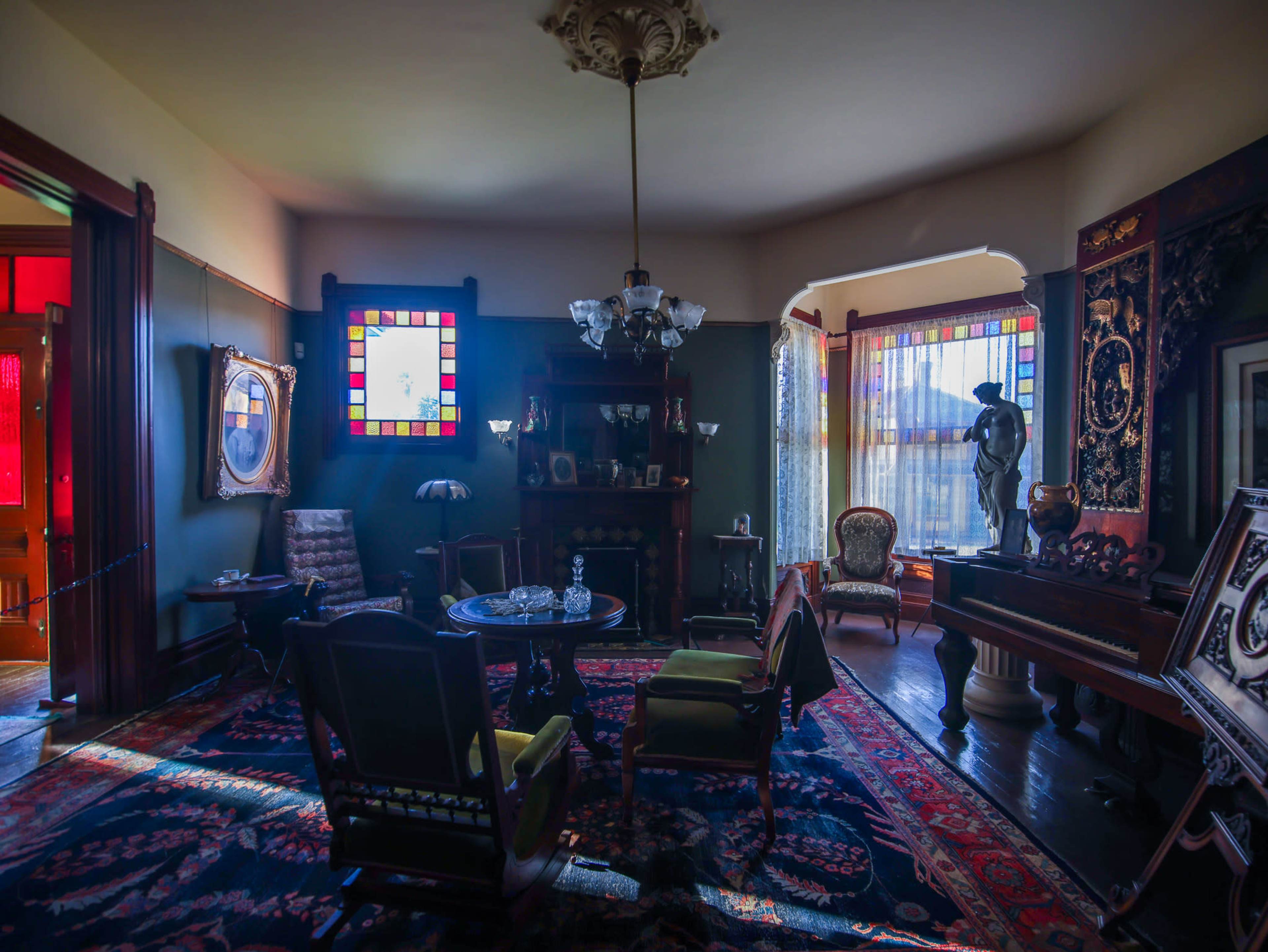 The interior of a vintage living room features ornate furniture, stained glass windows, and a chandelier.