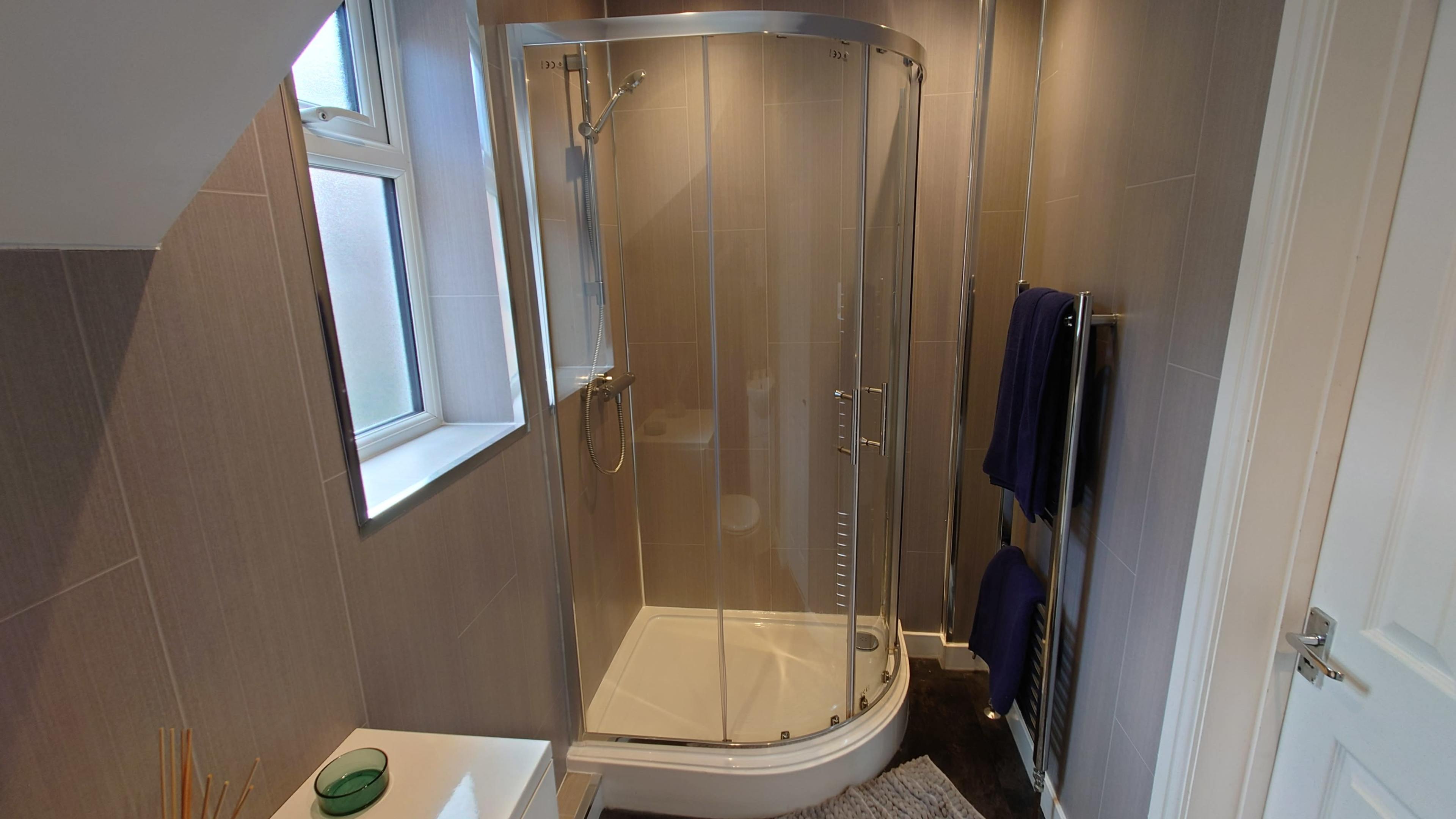 A modern, enclosed shower with a glass door, situated in a bathroom with neutral tile walls and dark flooring.