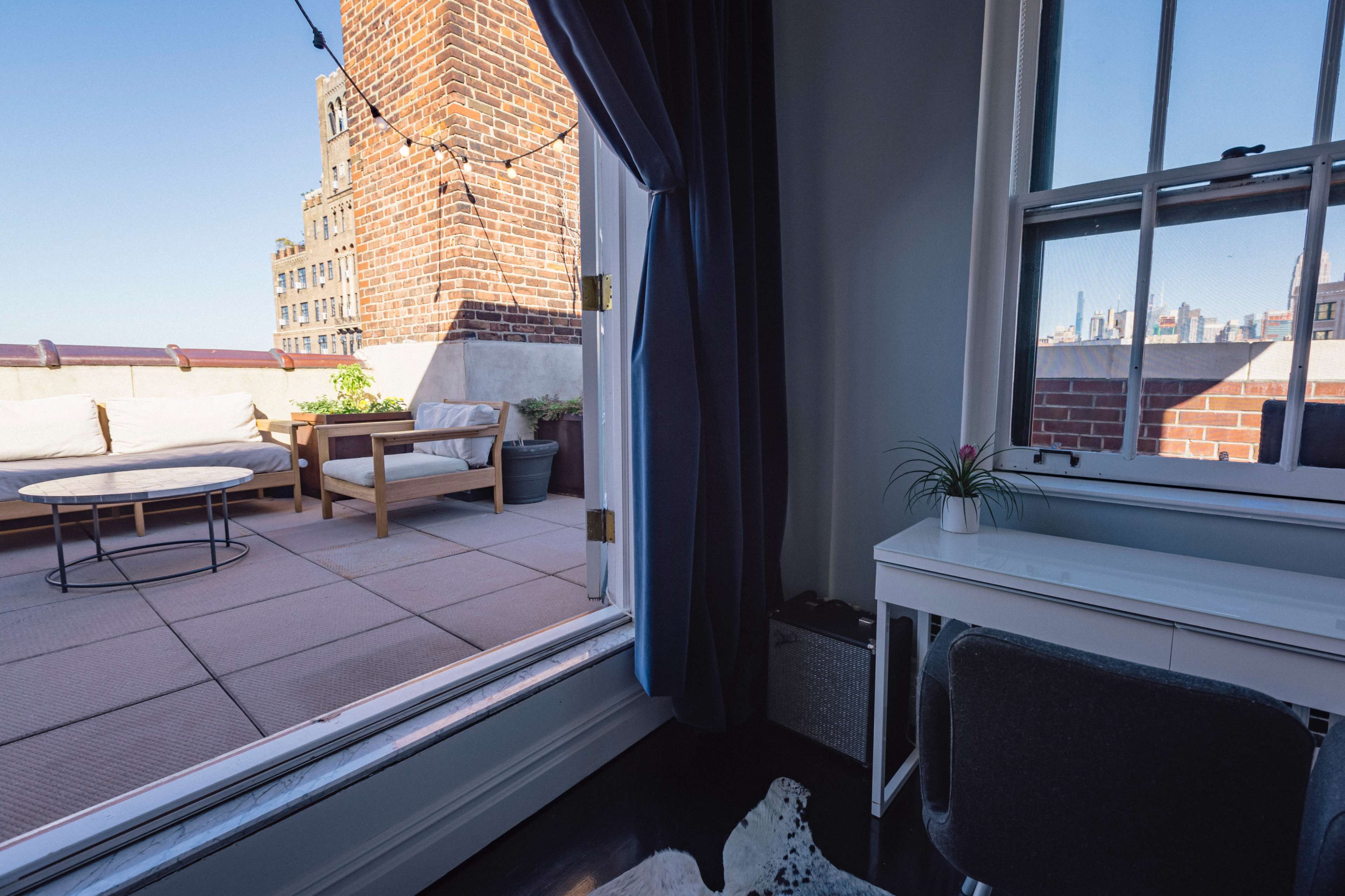 A spacious balcony with seating and potted plants is visible through an open window in a contemporary interior.