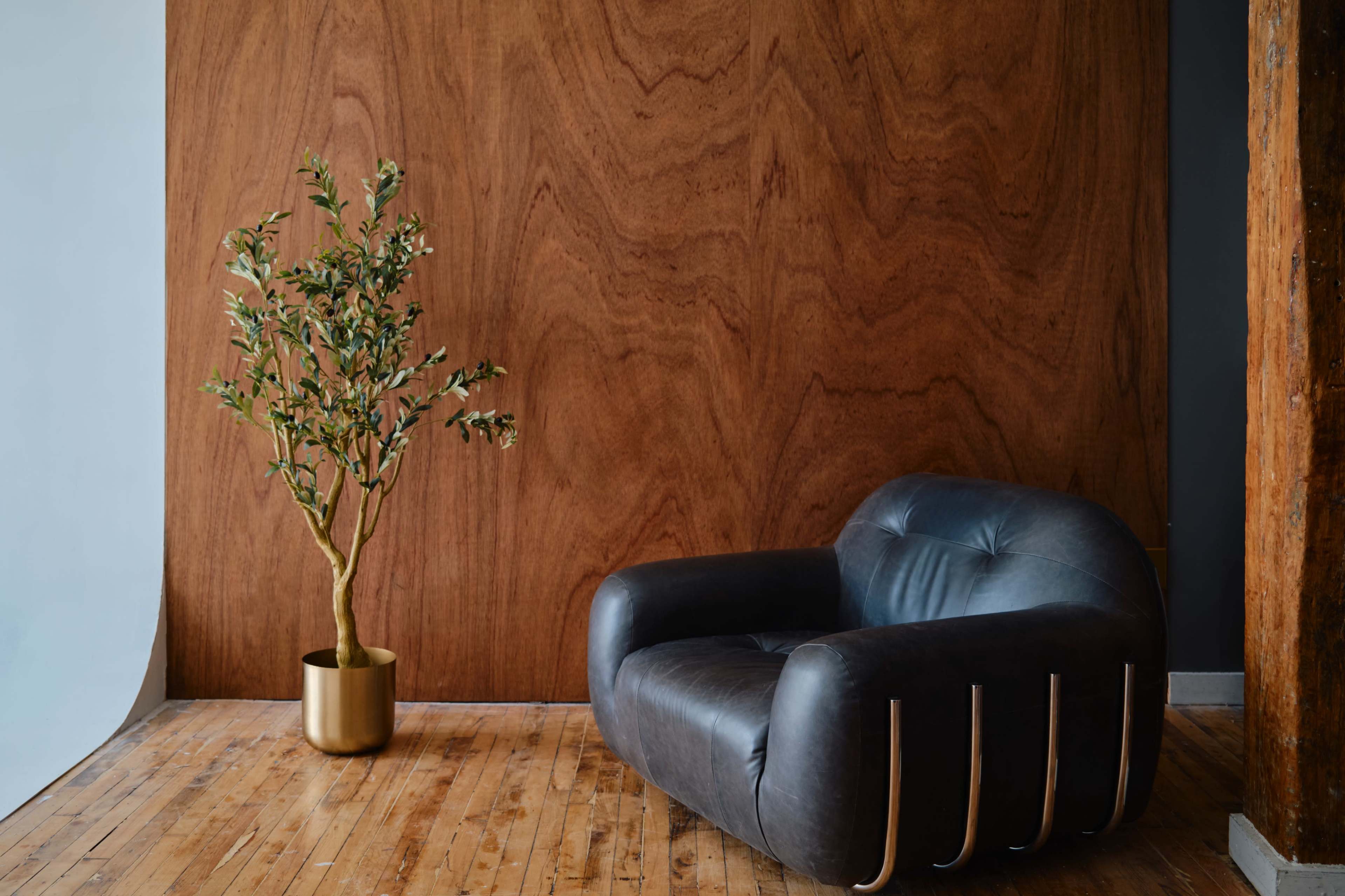 A black leather armchair is positioned against a textured wooden wall, with a small potted plant nearby.