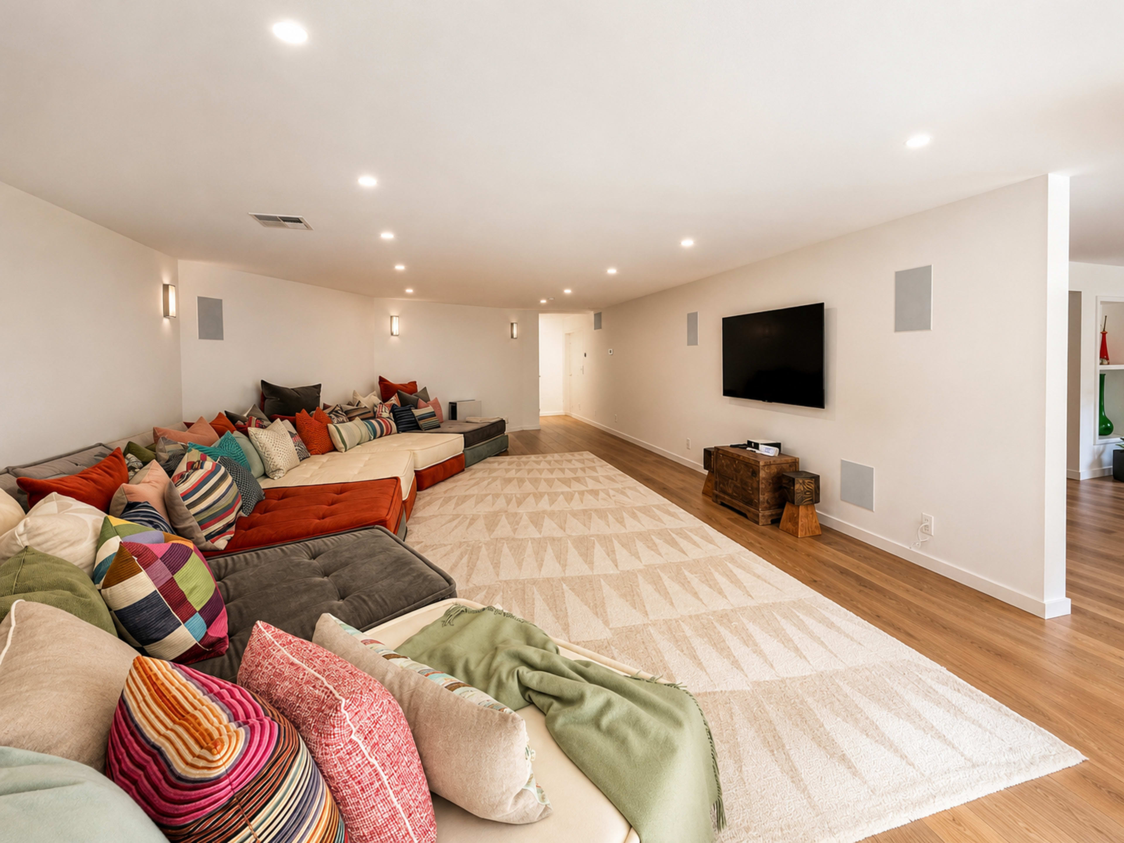 A spacious, modern living room features a large sectional sofa adorned with colorful pillows, a light-toned area rug, and a wall-mounted television.