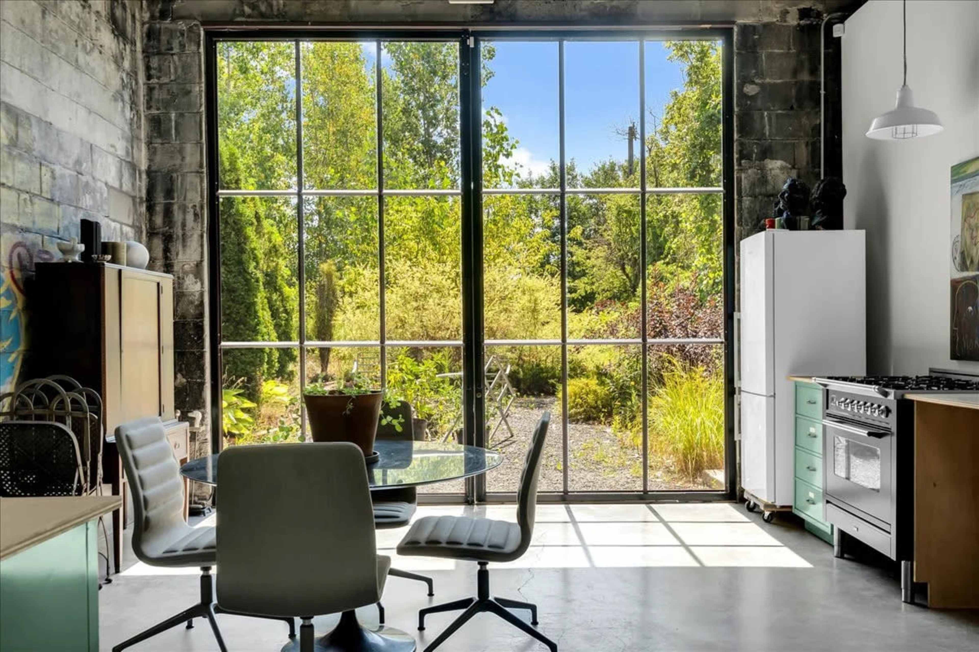 The image shows a modern kitchen and dining area with a large window that offers a view of a lush garden outside.