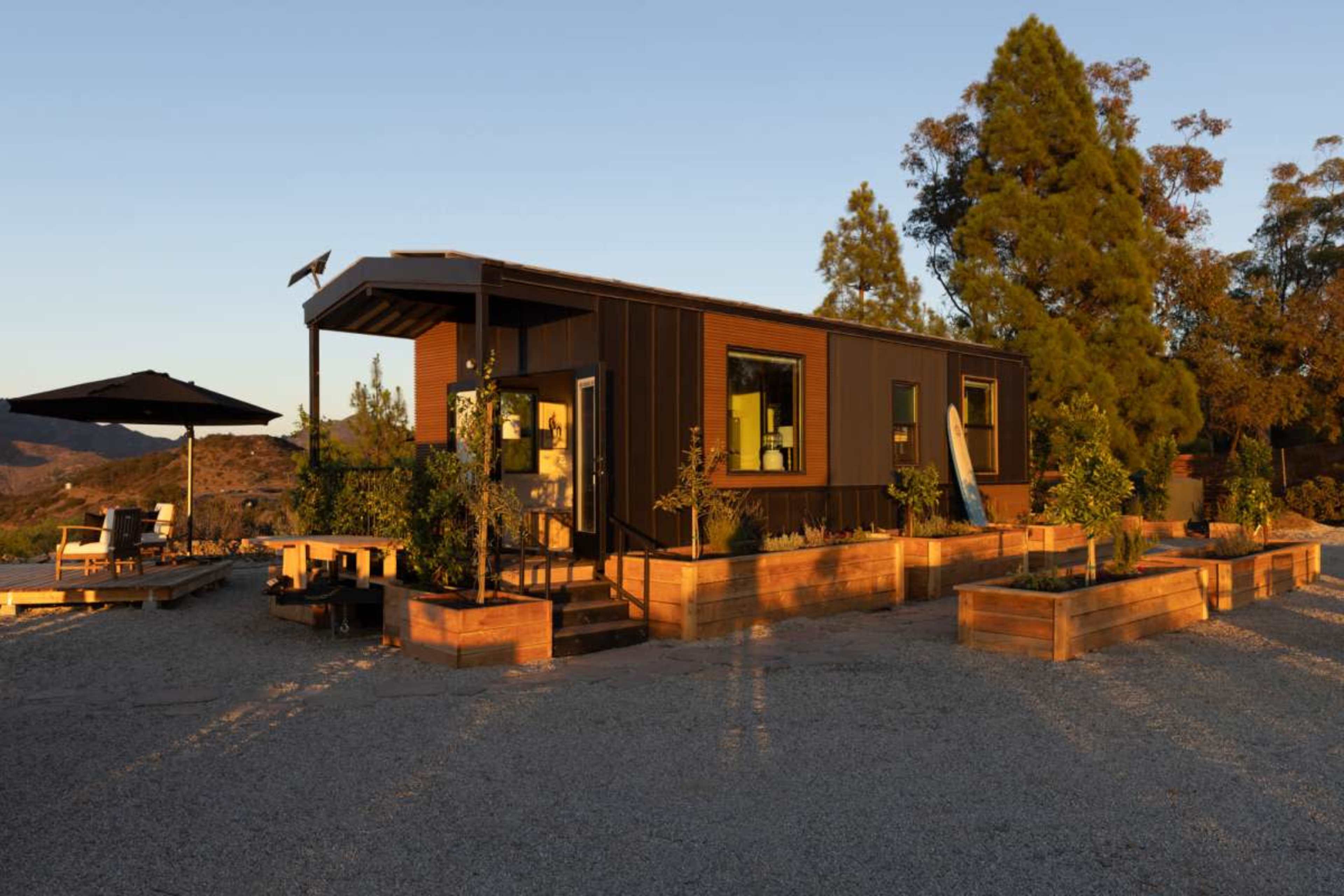 A modern, single-story home with a wooden deck is surrounded by landscaped planter boxes in a mountainous setting.