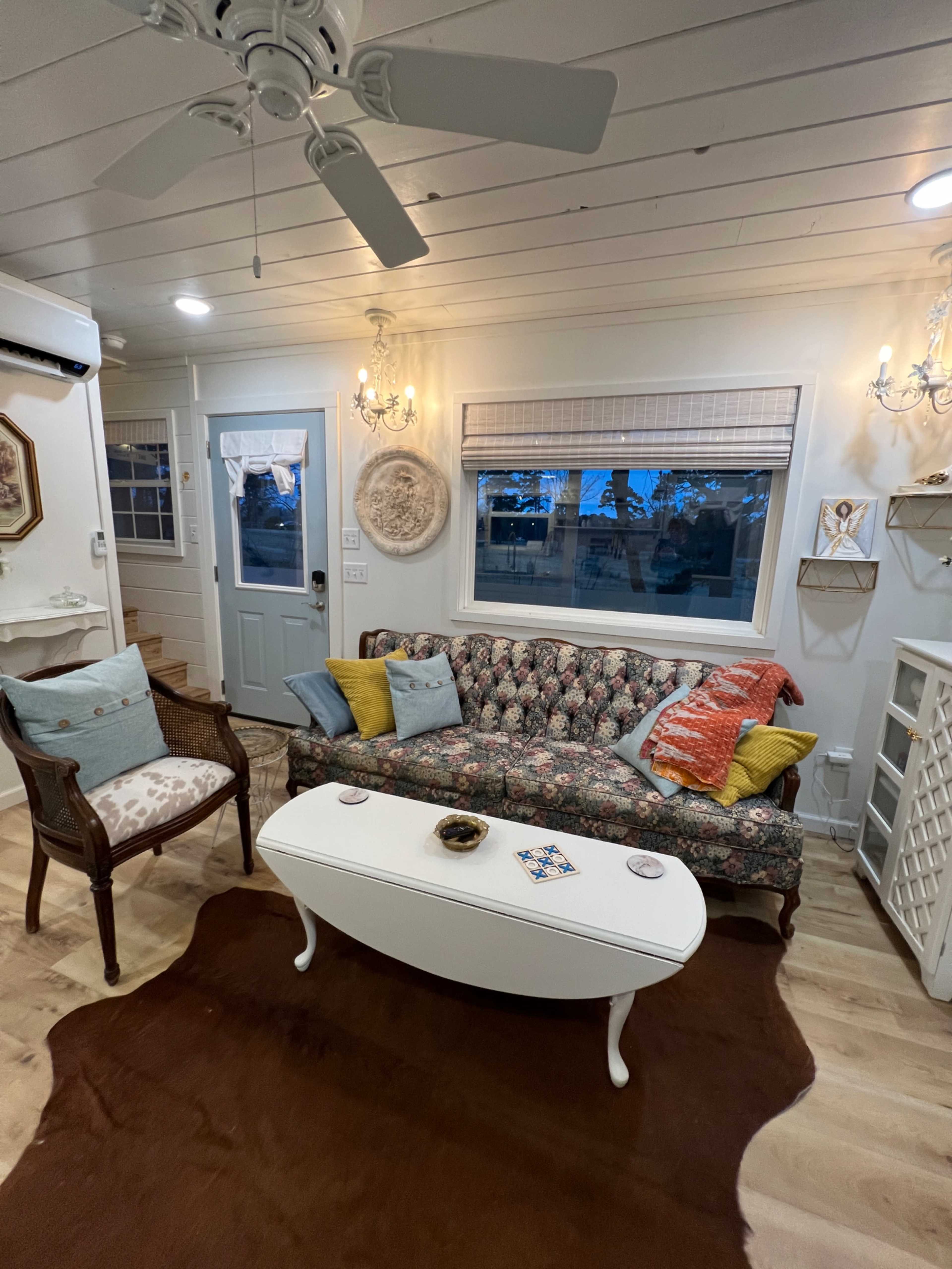 A living room with a floral-patterned sofa, a white coffee table, and a wooden chair, all arranged on a light-colored floor.