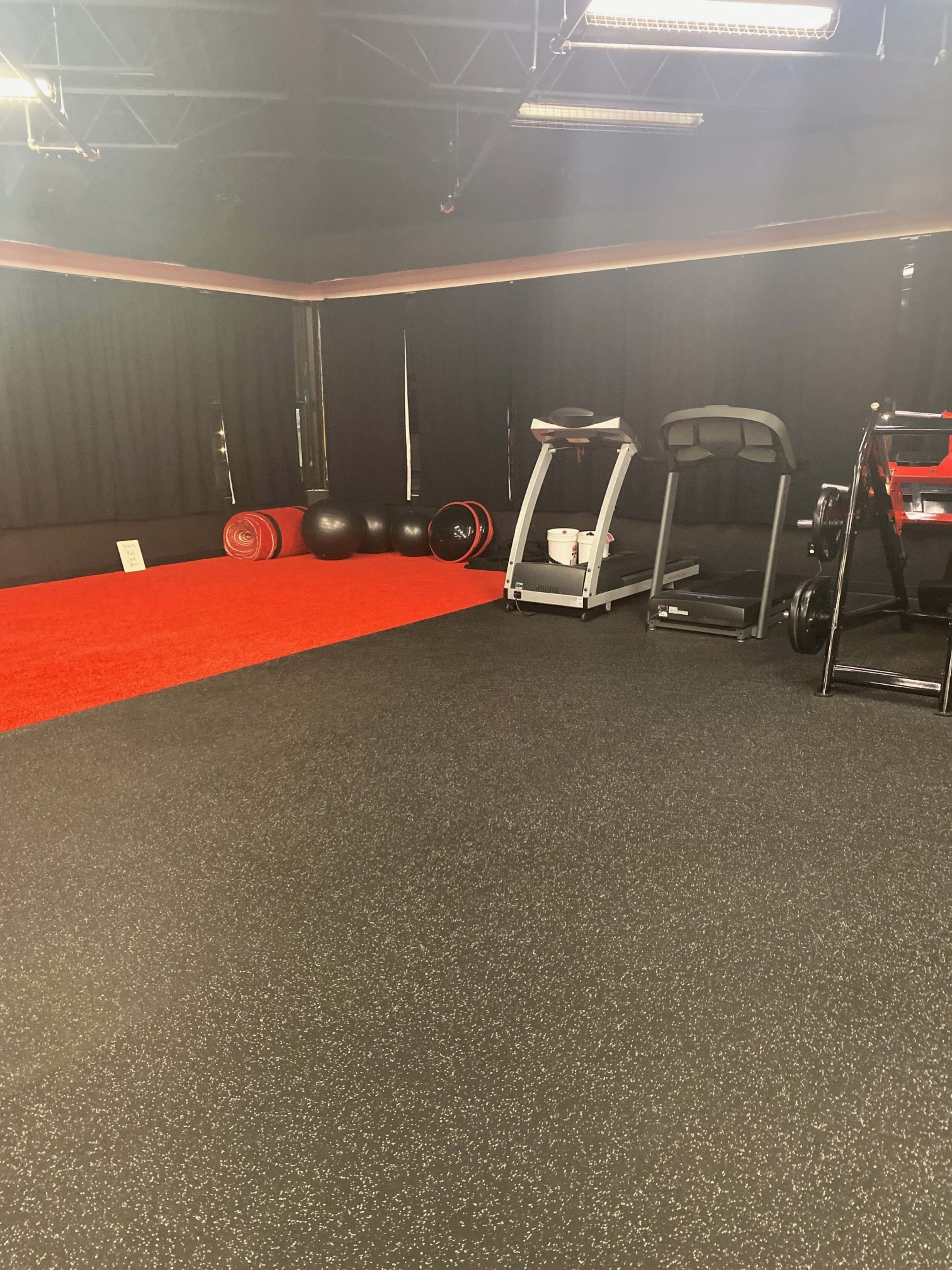 A gym interior with a red carpeted area, exercise equipment, and black curtains along the walls.
