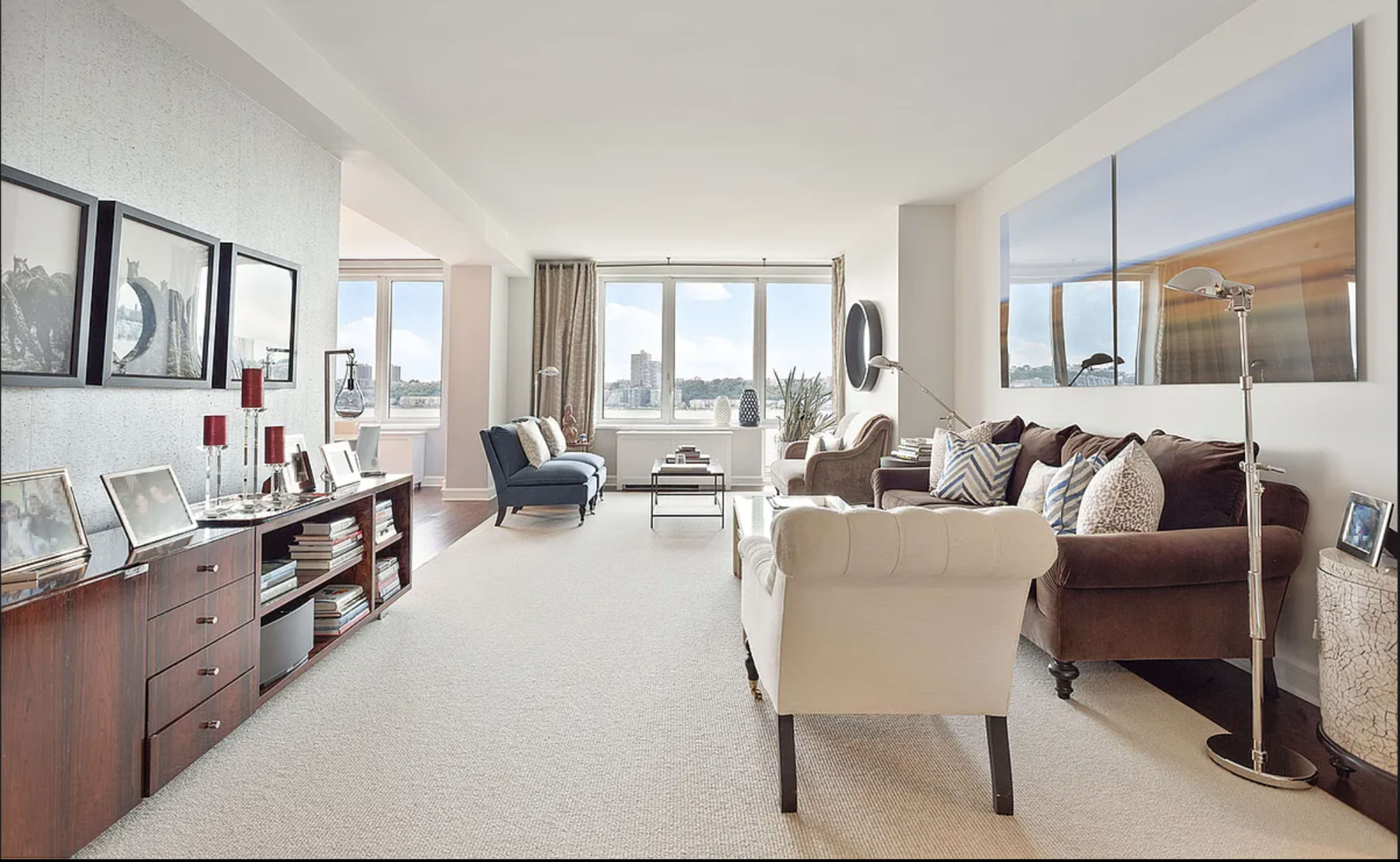 A modern living room with a light-colored carpet, two sofas, a coffee table, and large windows offering a view of the outdoors.