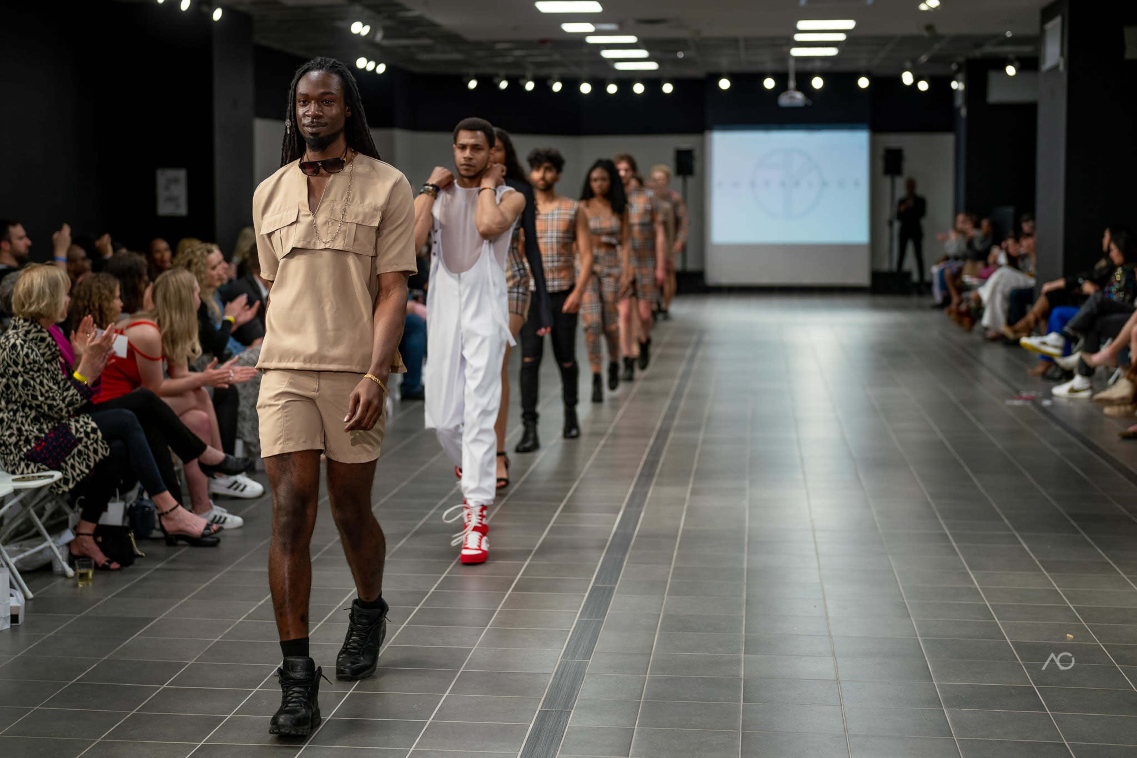Models walk down a runway during a fashion show, showcasing a variety of apparel styles.