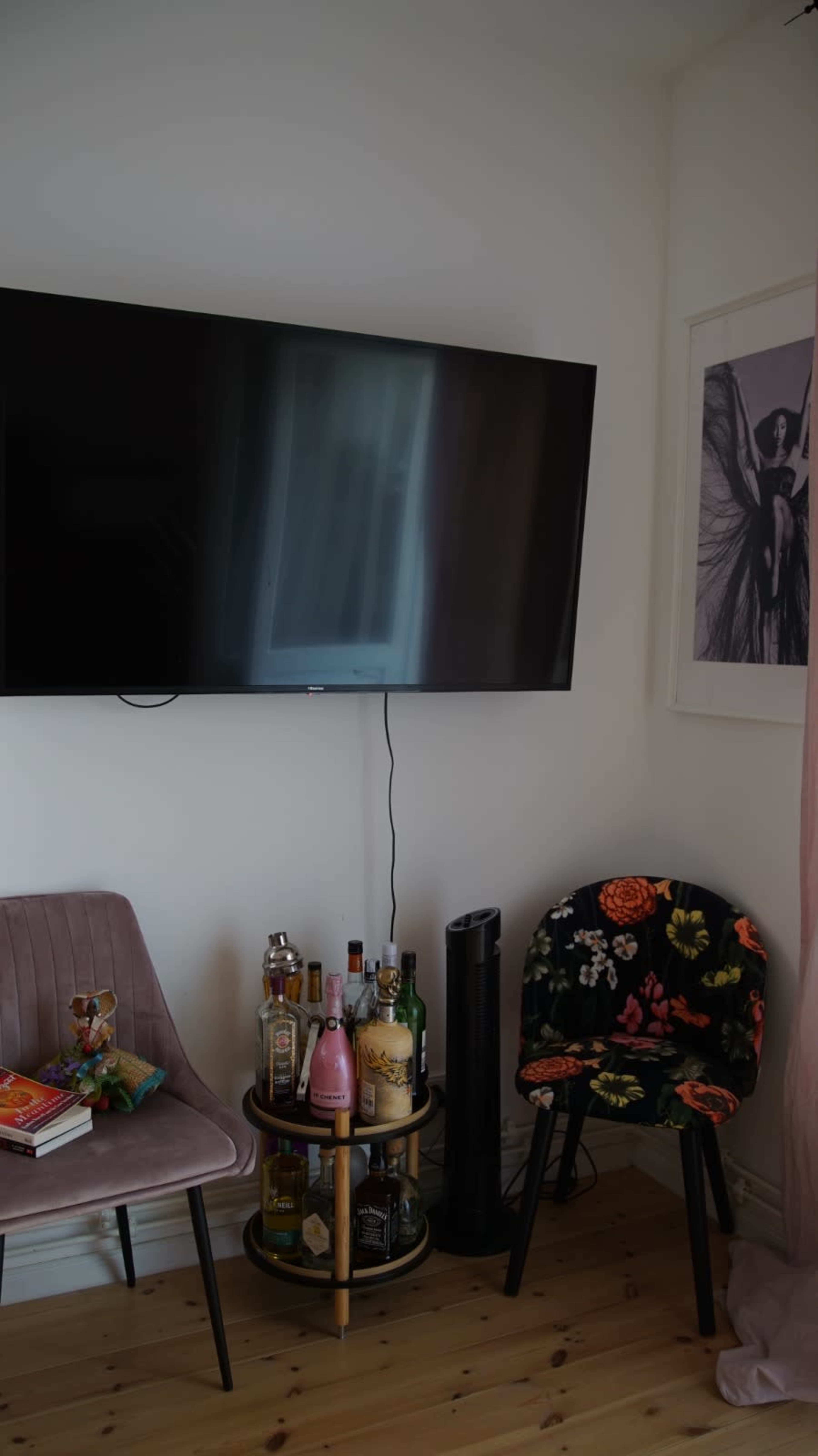 A small living area features a mounted television, two chairs, and a cart displaying various bottles of alcohol.