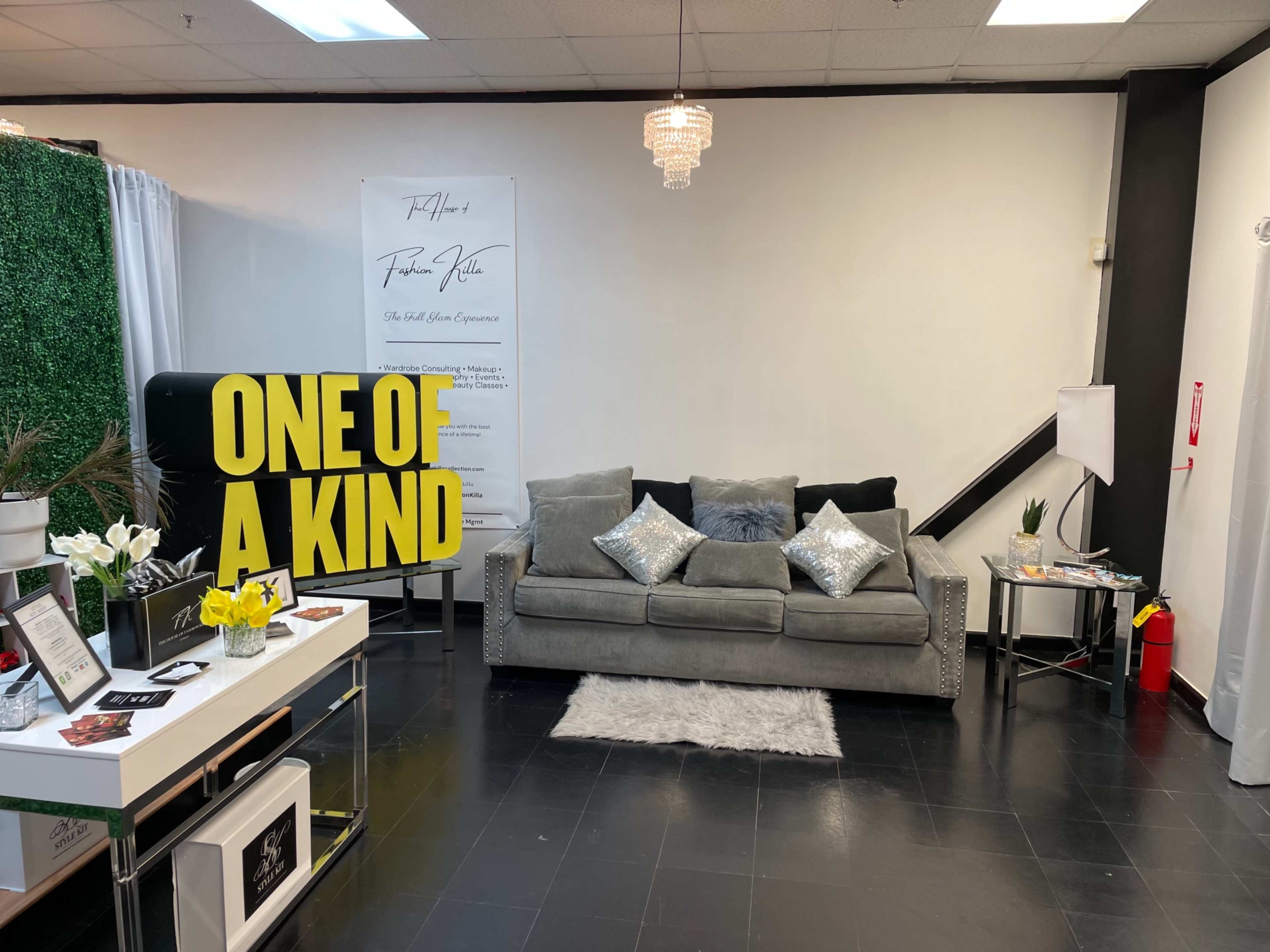 The image shows a modern lounge area with a gray sofa, decorative pillows, a small rug, and a large sign that reads "ONE OF A KIND" in bold letters.