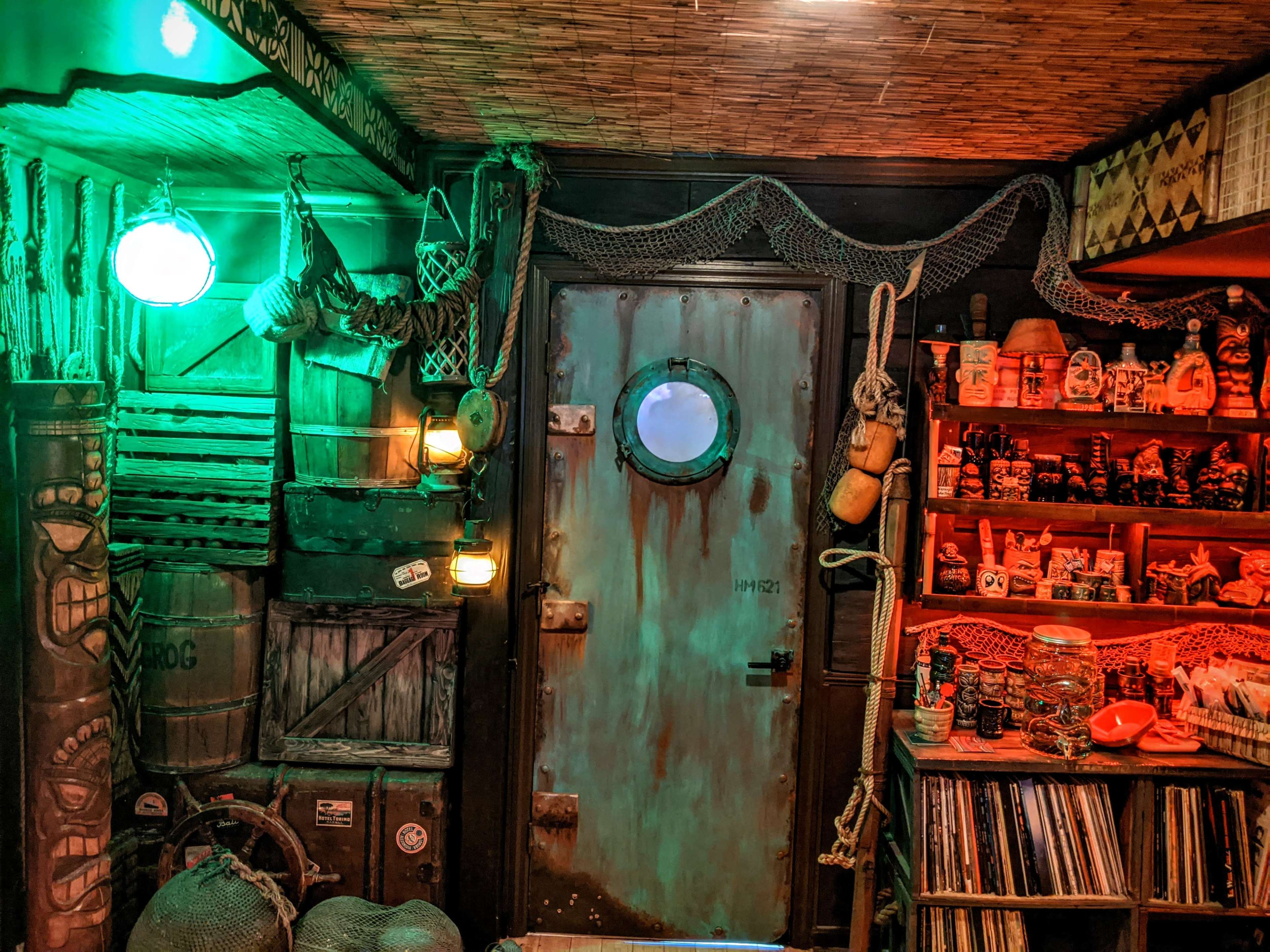 The image depicts a dimly lit, themed room featuring a porthole door, various nautical decorations, and shelves filled with collectibles.