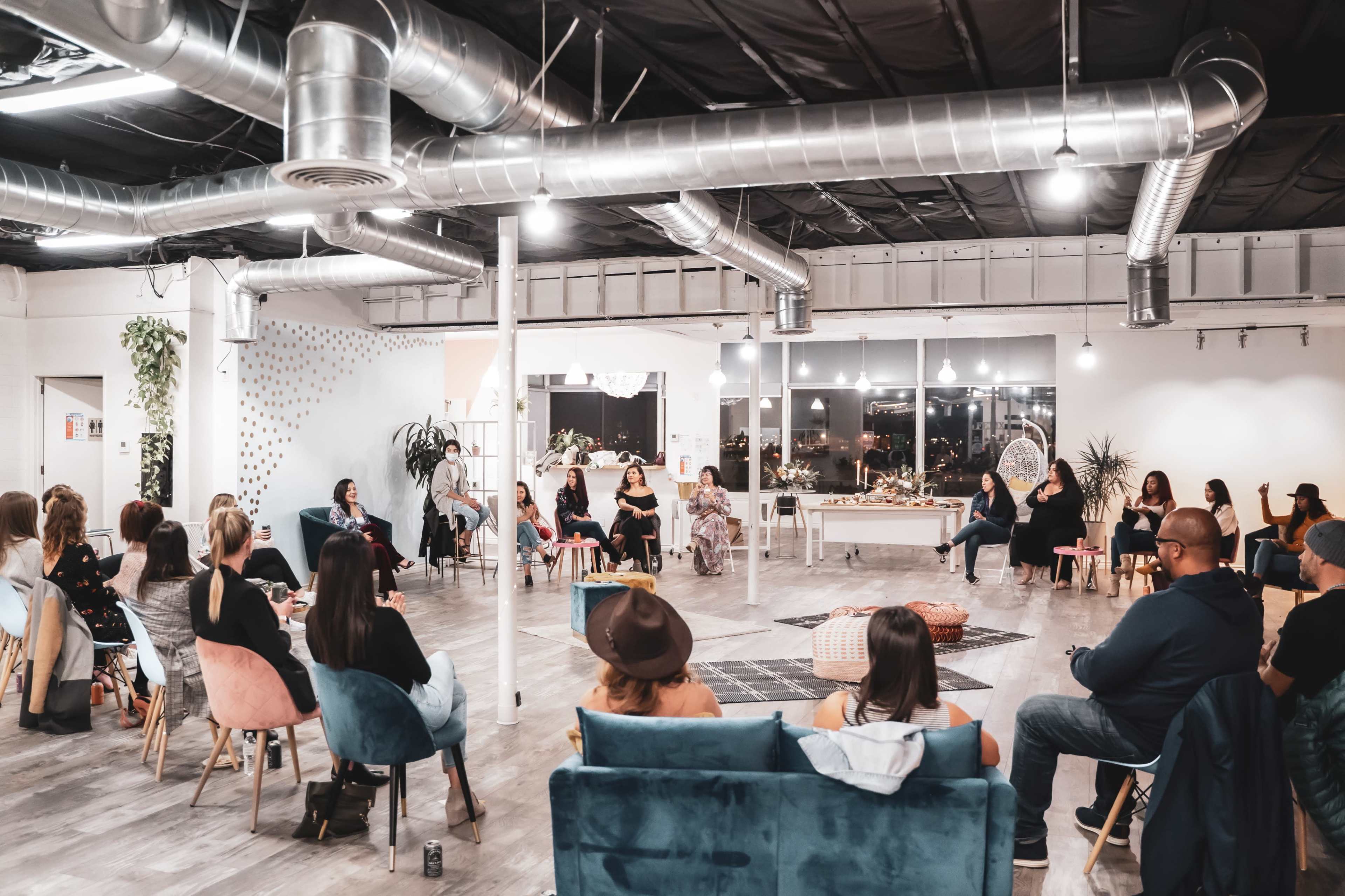A group of people sit in a modern, open space with seating arranged in a circular formation for a gathering or meeting.