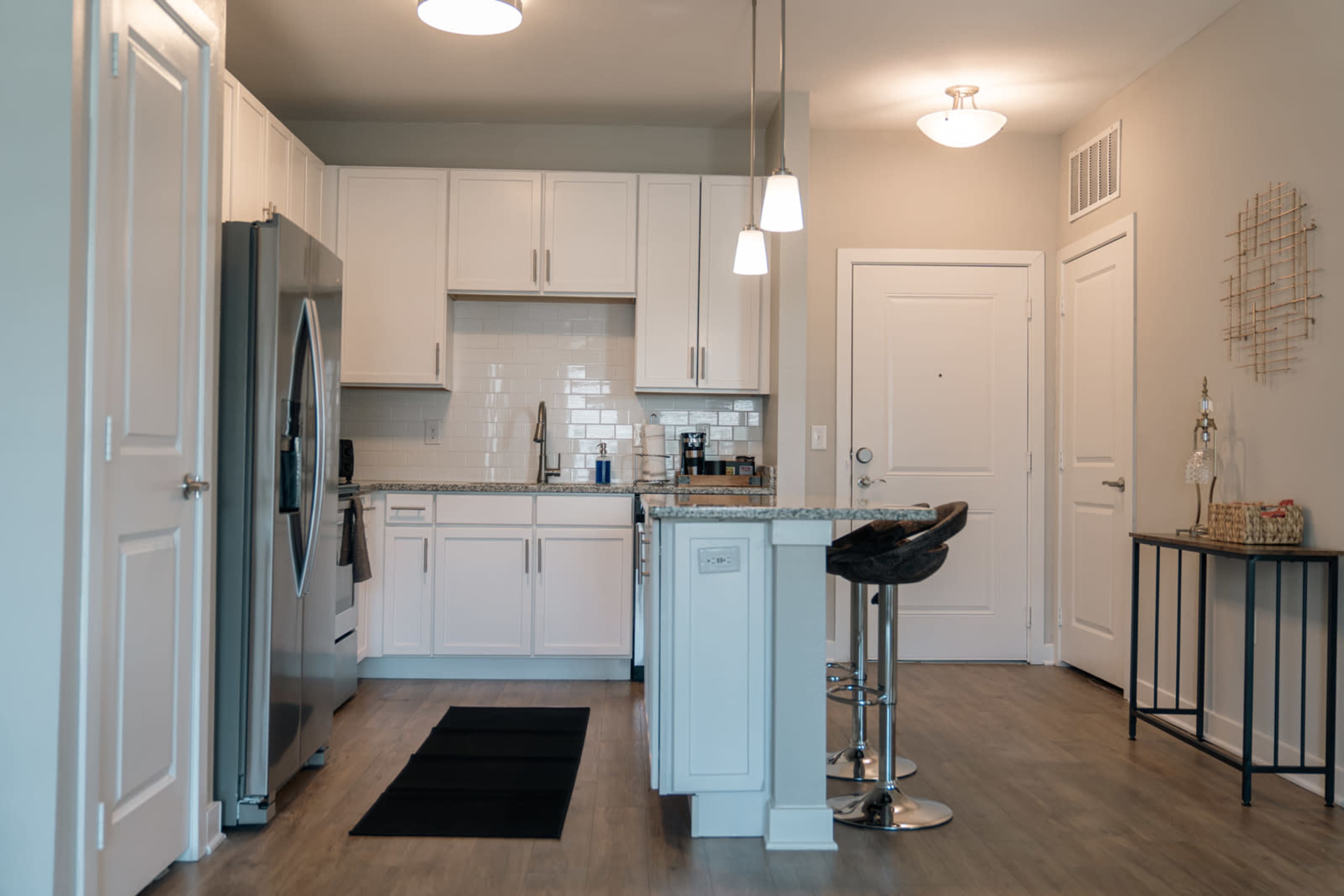 A modern kitchen features white cabinetry, stainless steel appliances, and a small dining area with bar stools.