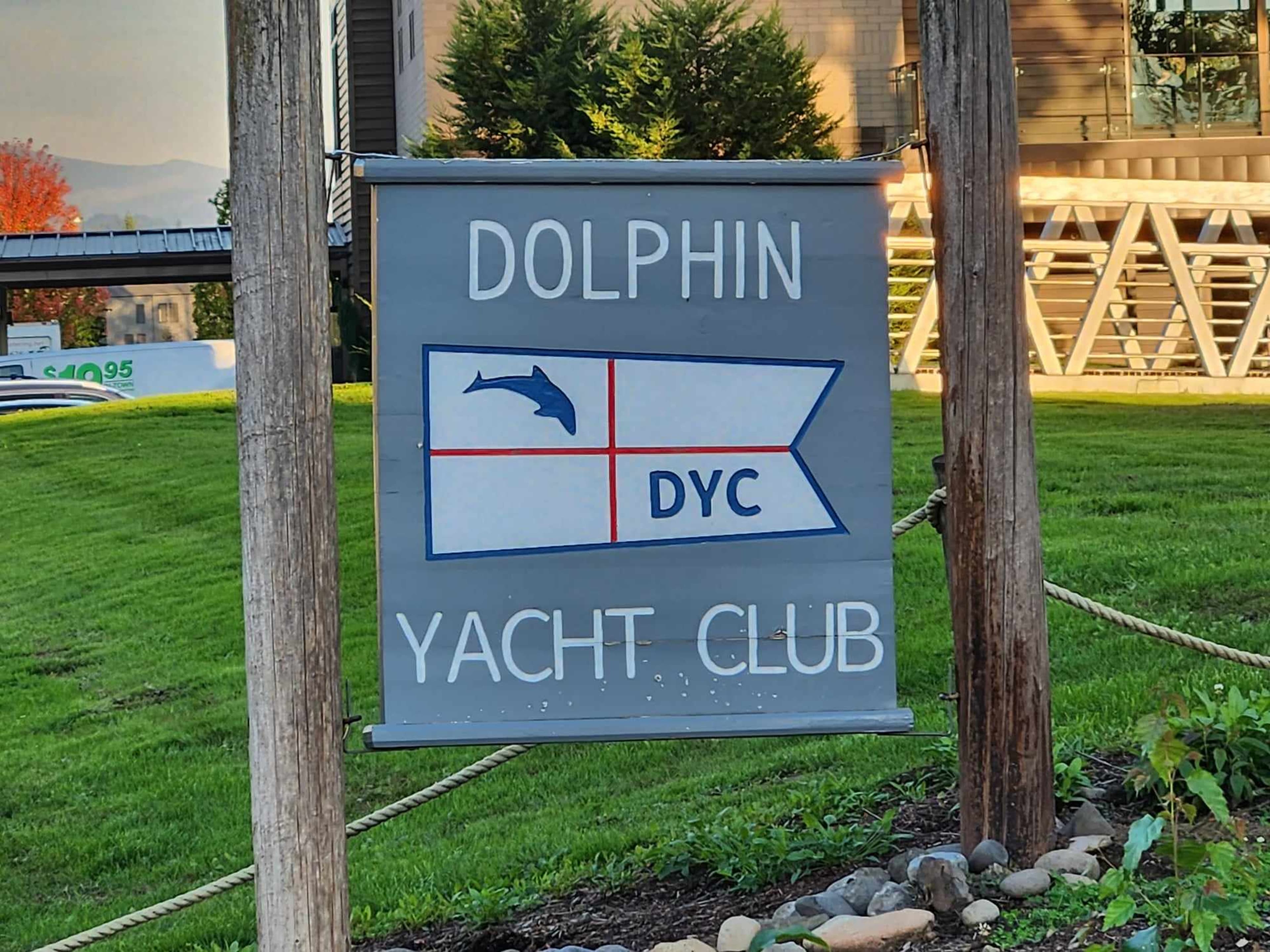 The image shows a sign for the Dolphin Yacht Club featuring a flag design with a dolphin and the letters "DYC" on it.