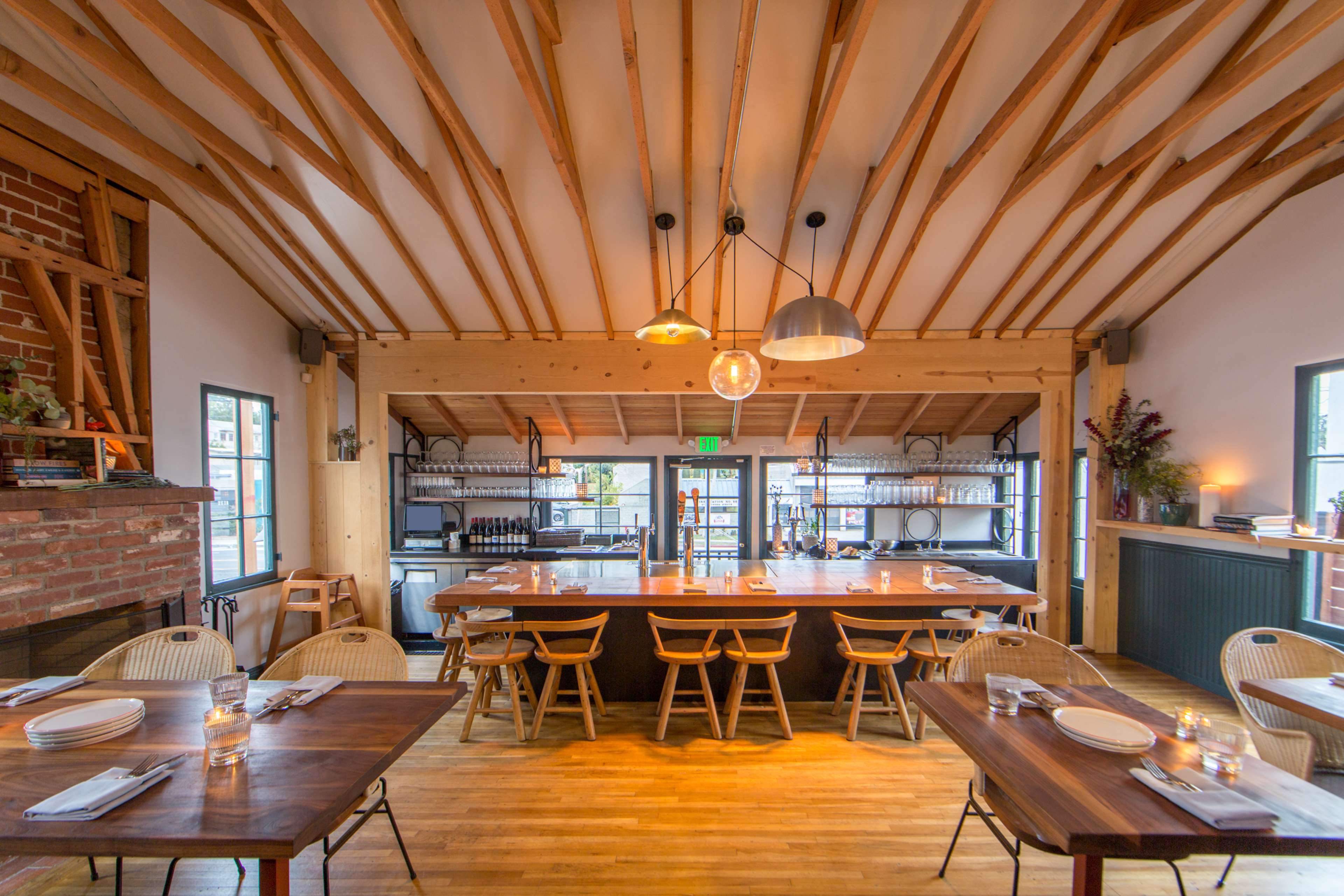 The image shows a modern restaurant interior with wooden beams, a central bar area, and tables set for dining.