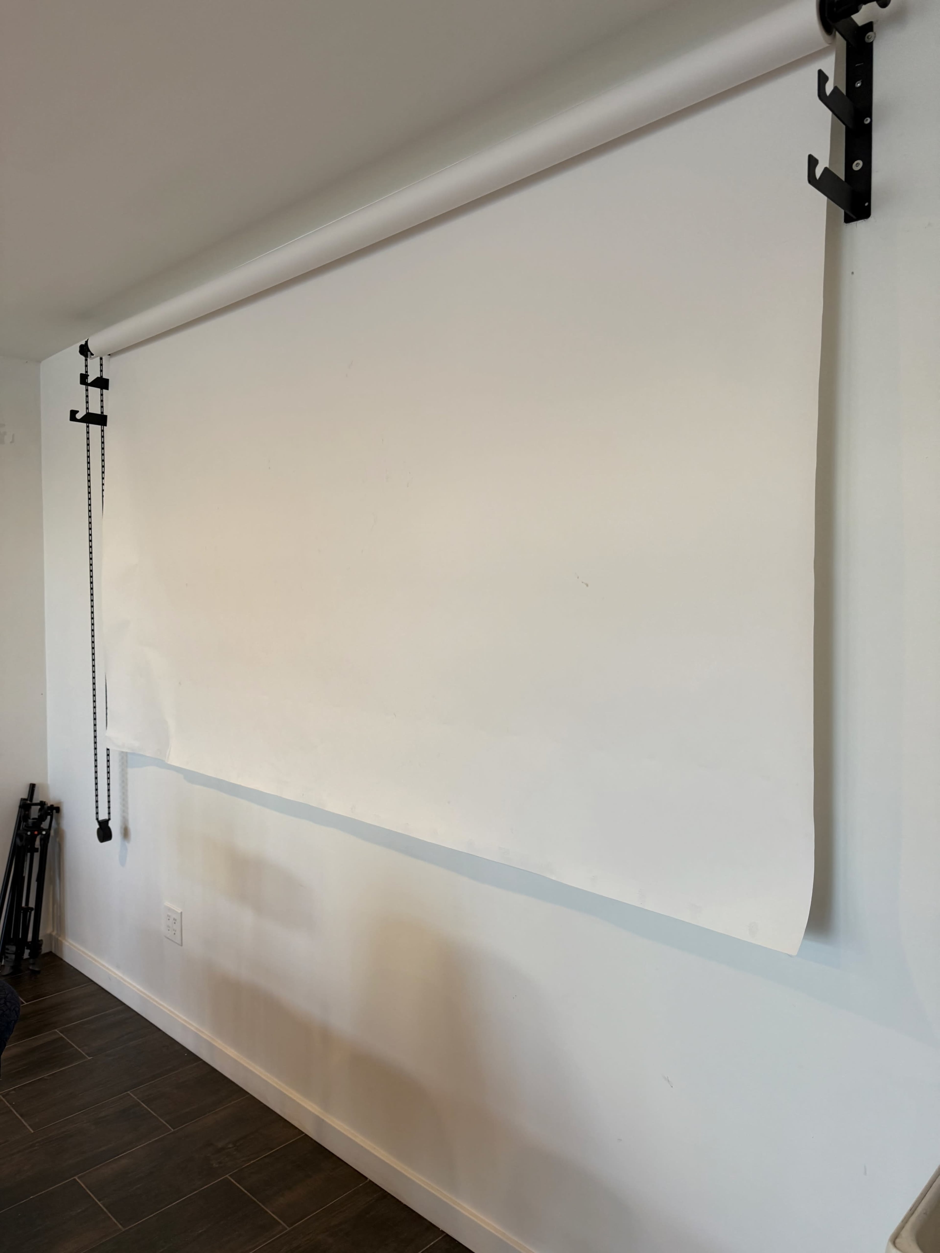 A large, blank paper backdrop is rolled down from a wall-mounted support in a well-lit room.
